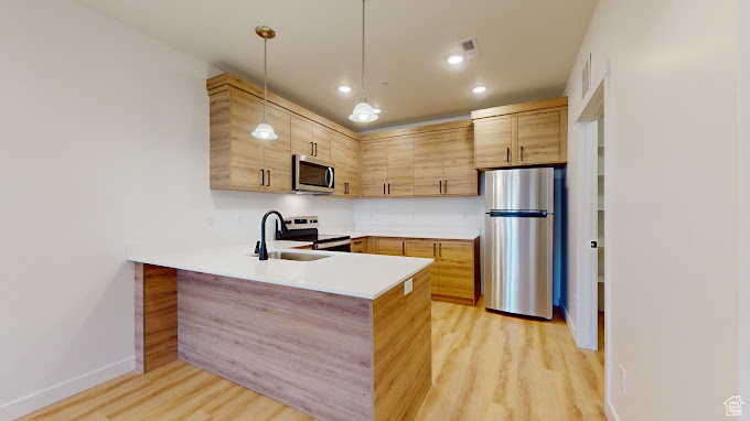 Kitchen featuring decorative light fixtures, stainless steel appliances, light wood-style floors, sink, and kitchen peninsula