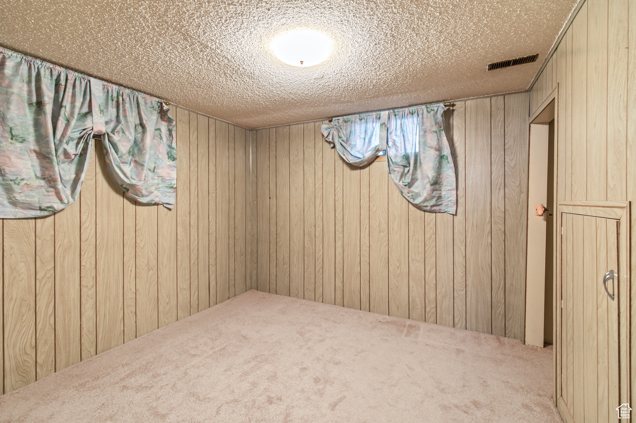 Carpeted empty room featuring a textured ceiling and wooden walls