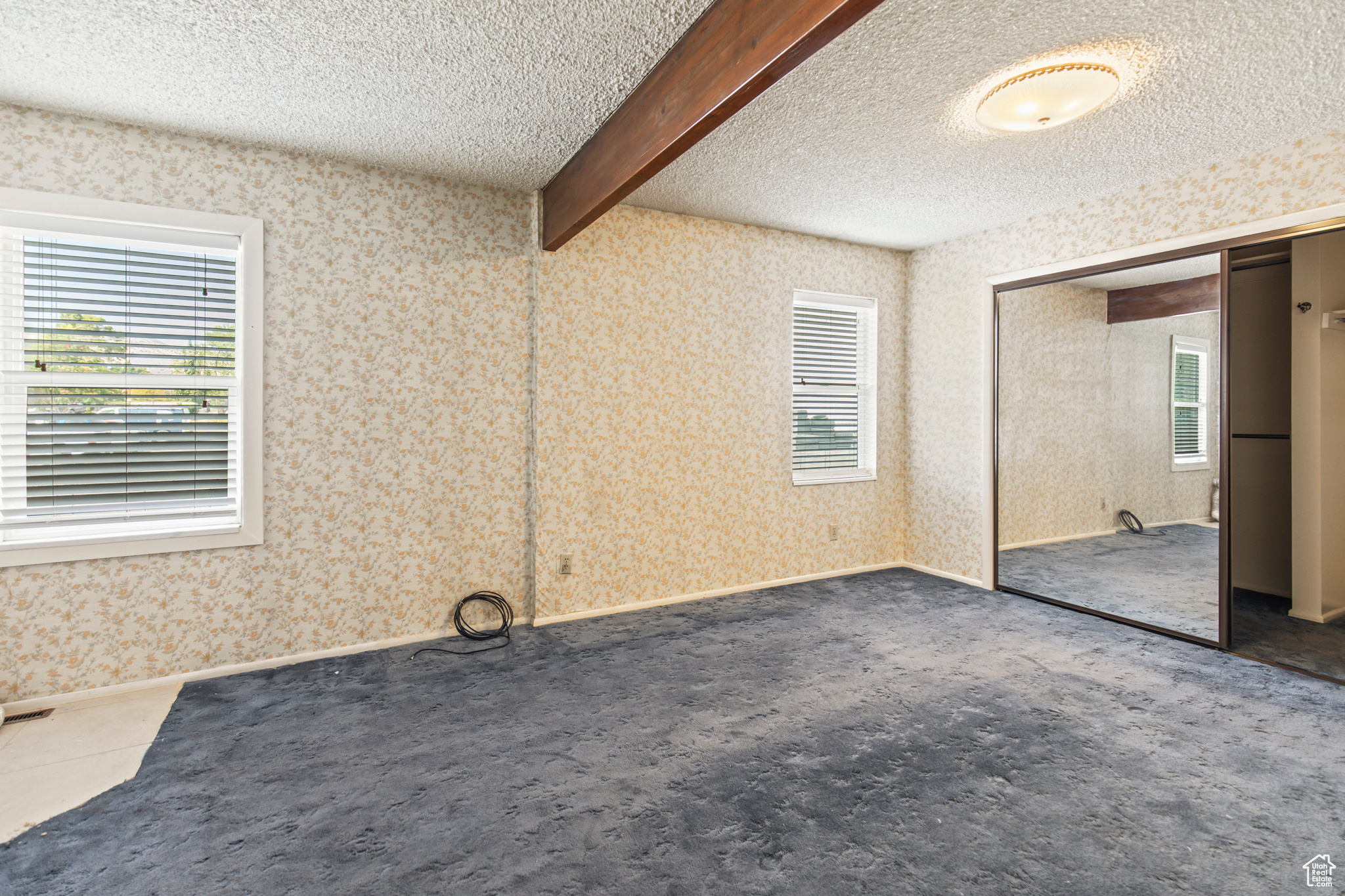 Carpeted empty room with beamed ceiling and a textured ceiling