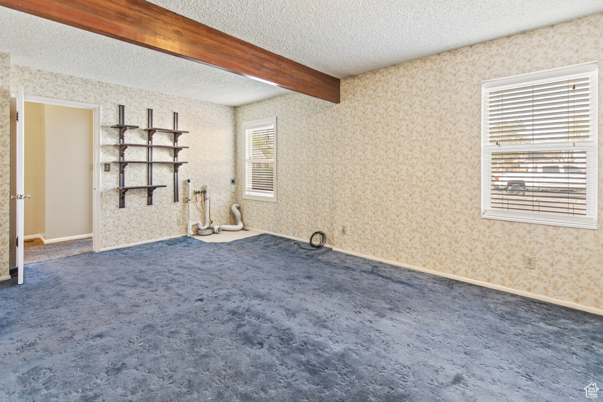 Carpeted empty room with a textured ceiling, a wealth of natural light, and beam ceiling