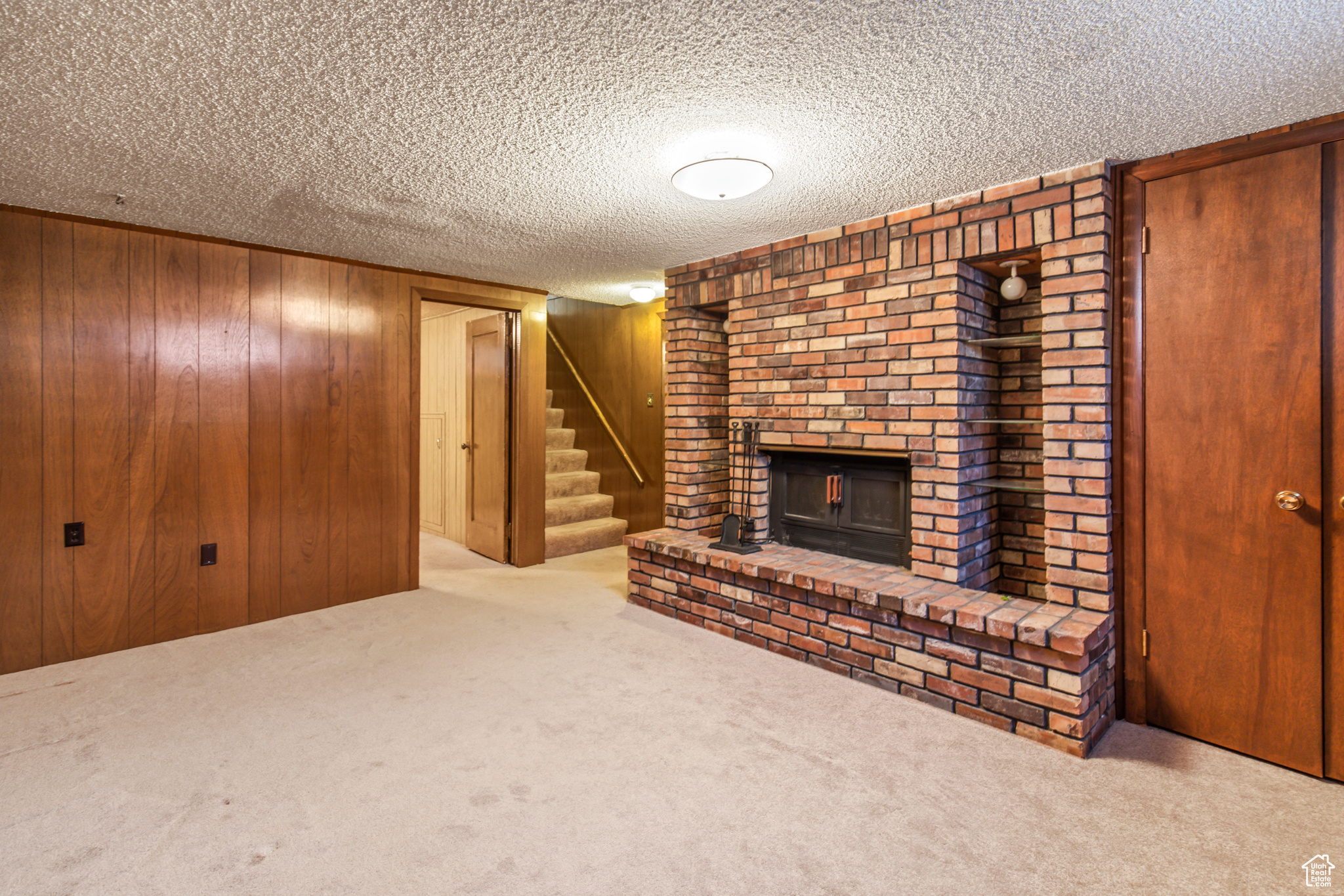 Unfurnished living room with wood walls, a fireplace, light carpet, and a textured ceiling