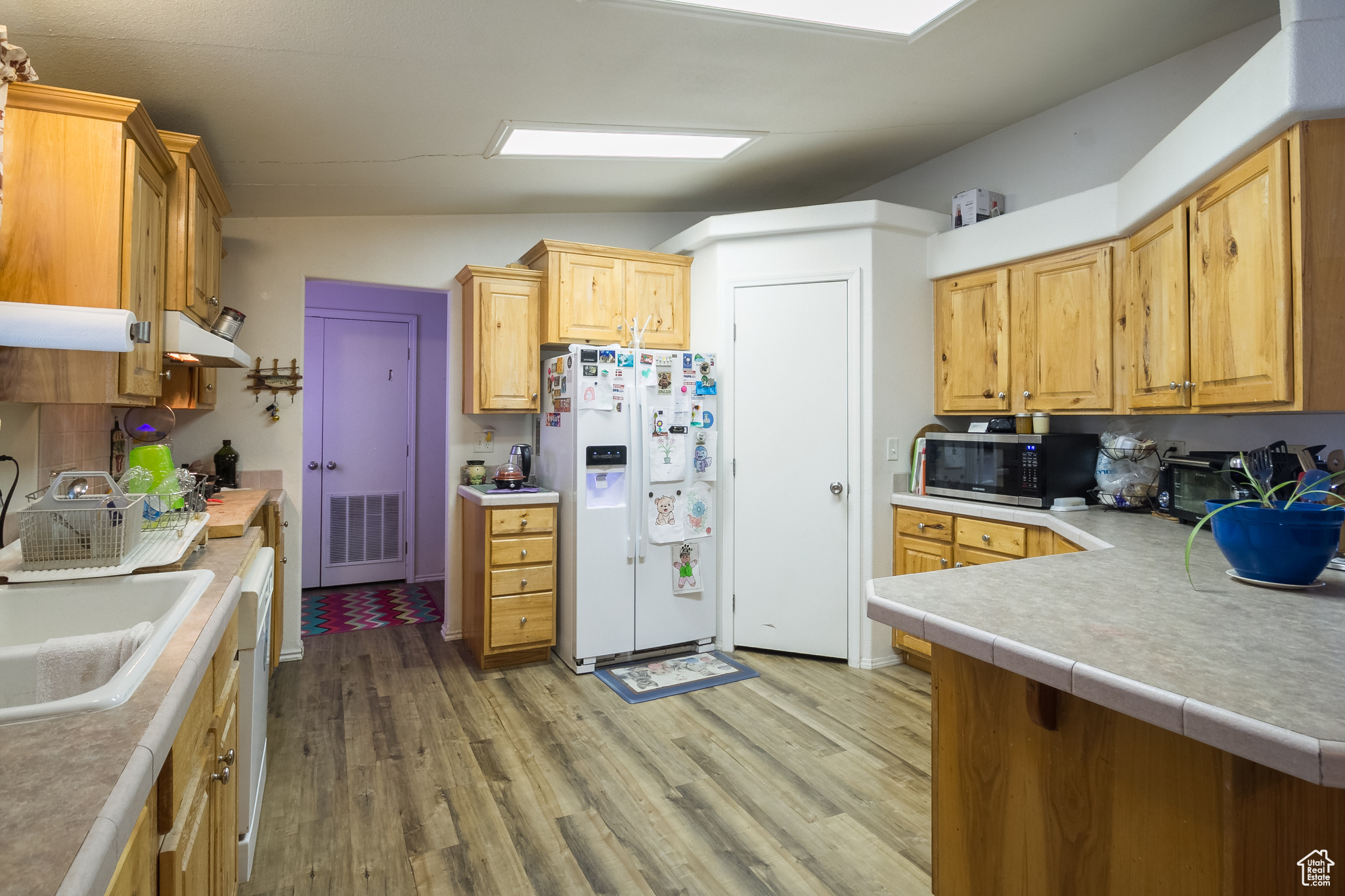 Kitchen with kitchen peninsula, light wood-type flooring, vaulted ceiling, sink, and white fridge with ice dispenser