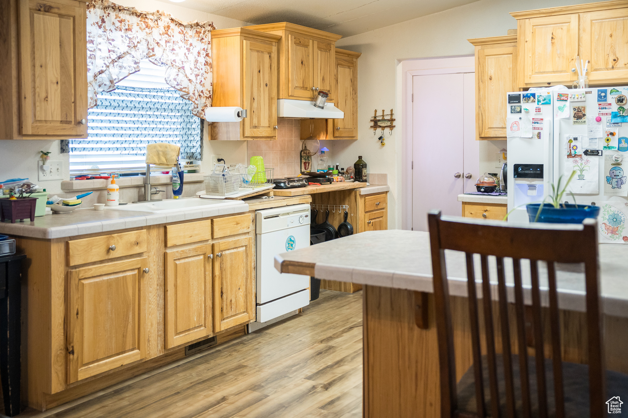 Kitchen with tile counters, light hardwood / wood-style flooring, white appliances, and sink