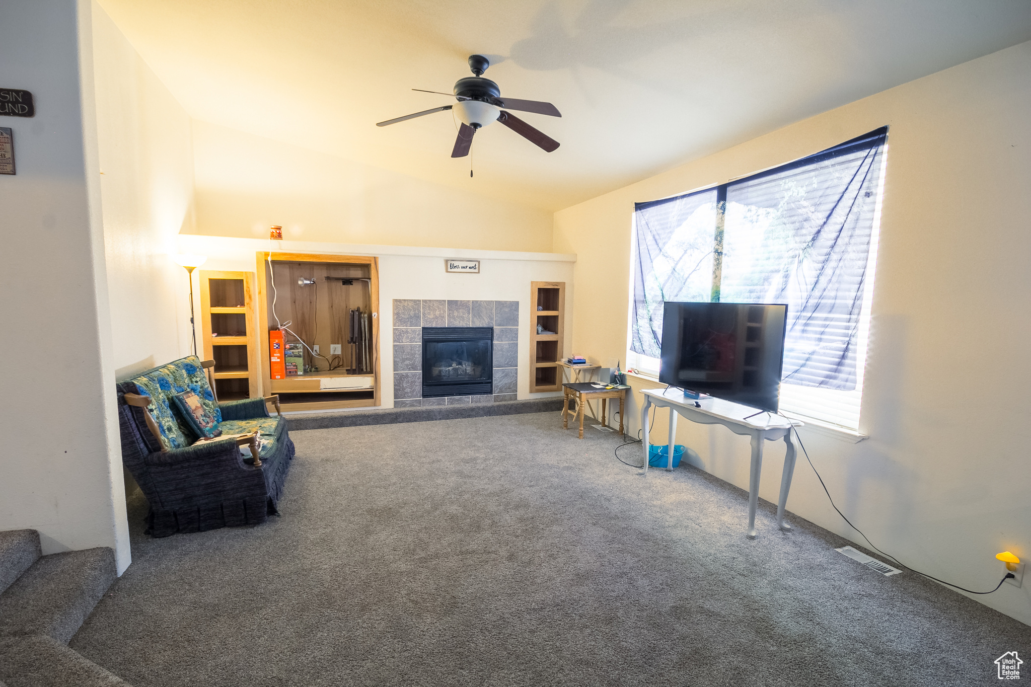 Living room featuring carpet, ceiling fan, lofted ceiling, and a tile fireplace