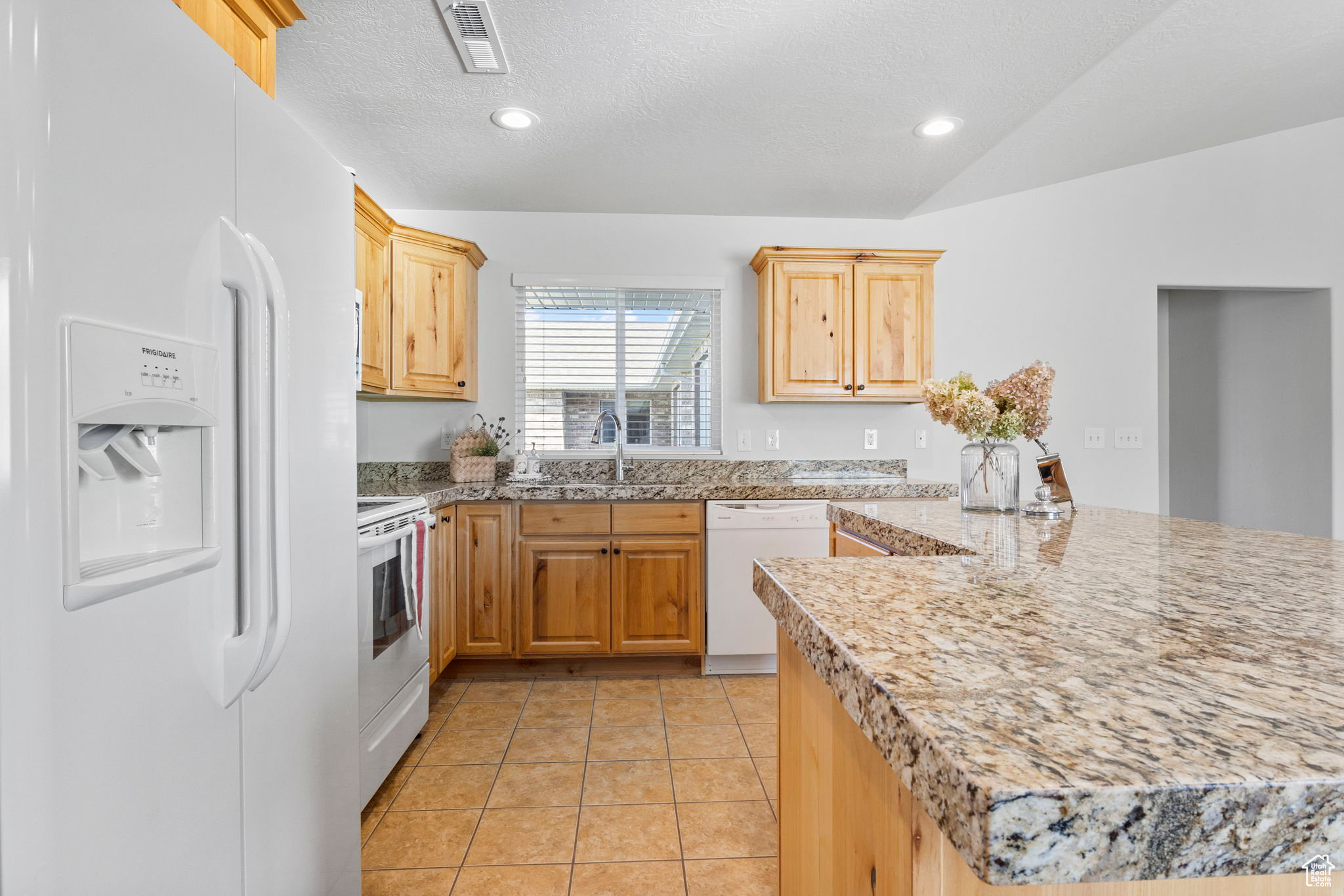 Kitchen with light brown cabinetry, white appliances, sink, lofted ceiling, and kitchen peninsula