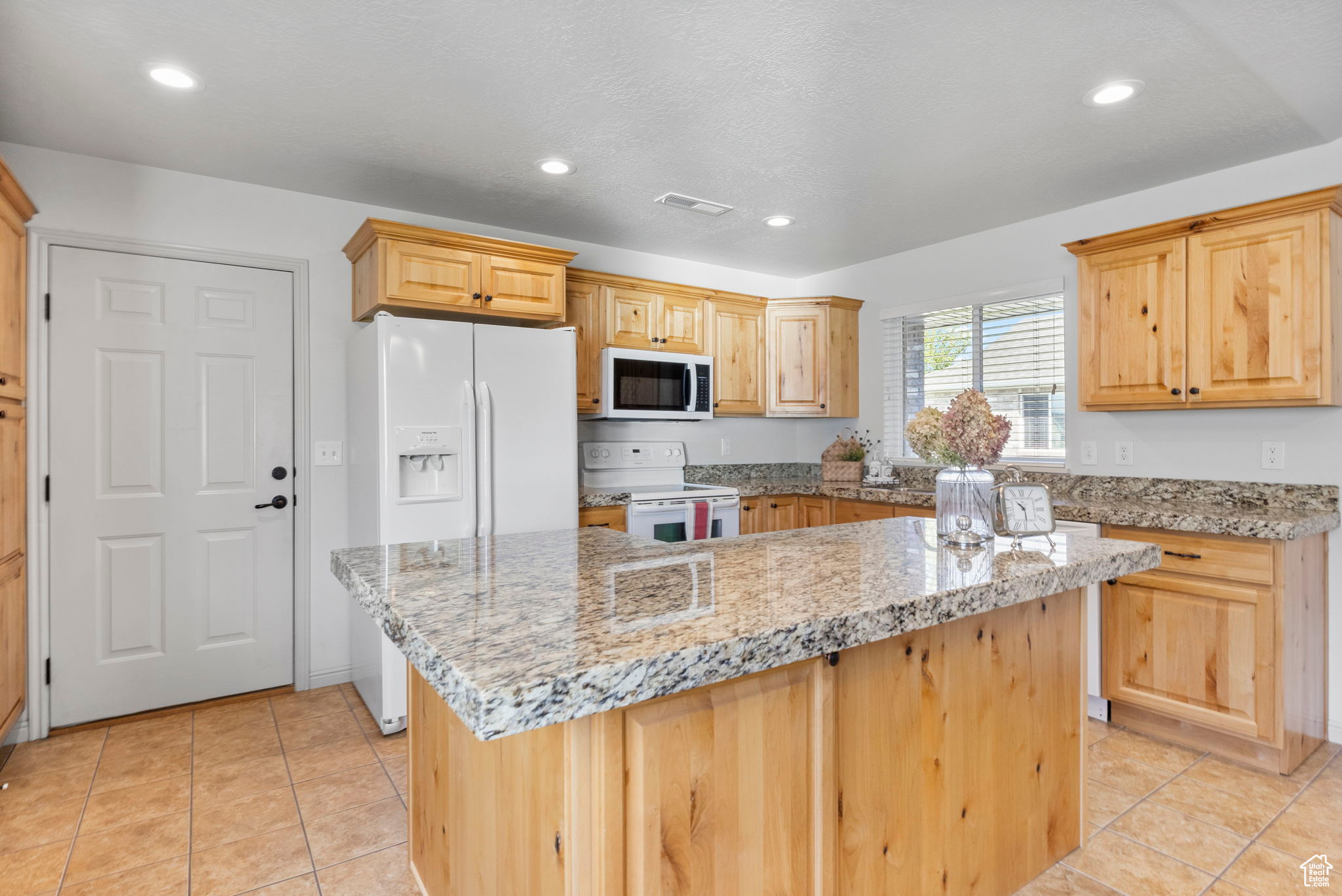 Kitchen featuring white appliances, light stone counters, and a kitchen island