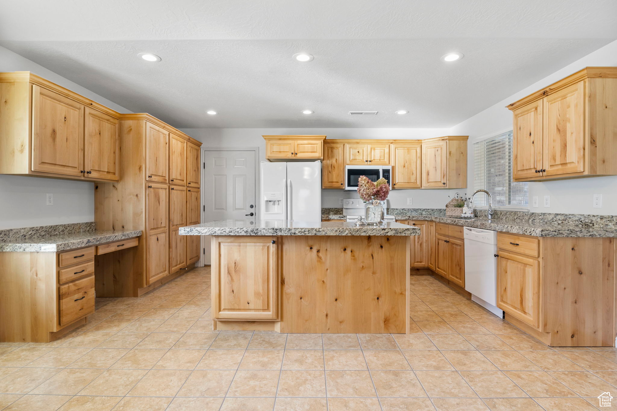 Kitchen with white appliances, light stone counters, and a center island