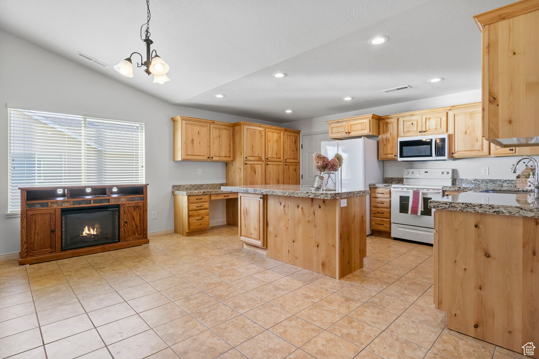 Kitchen featuring hanging light fixtures, white appliances, light stone counters, sink, and a kitchen island