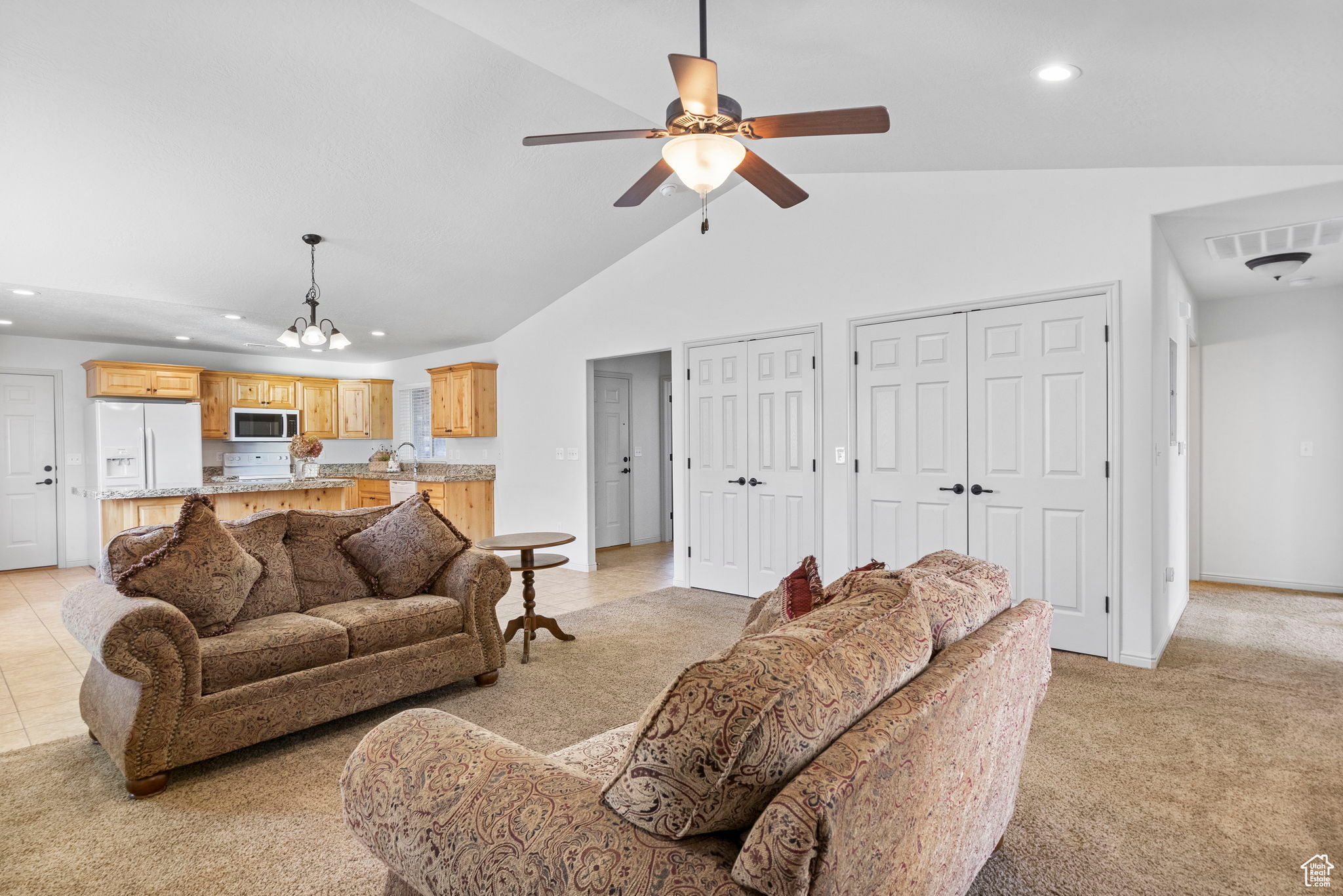 Living room featuring ceiling fan with notable chandelier, high vaulted ceiling, light tile patterned floors, and sink