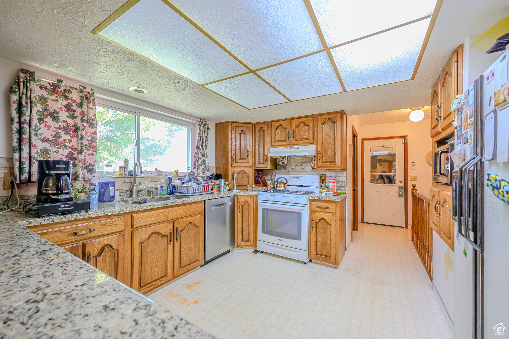 Kitchen featuring white appliances, light stone countertops, and sink