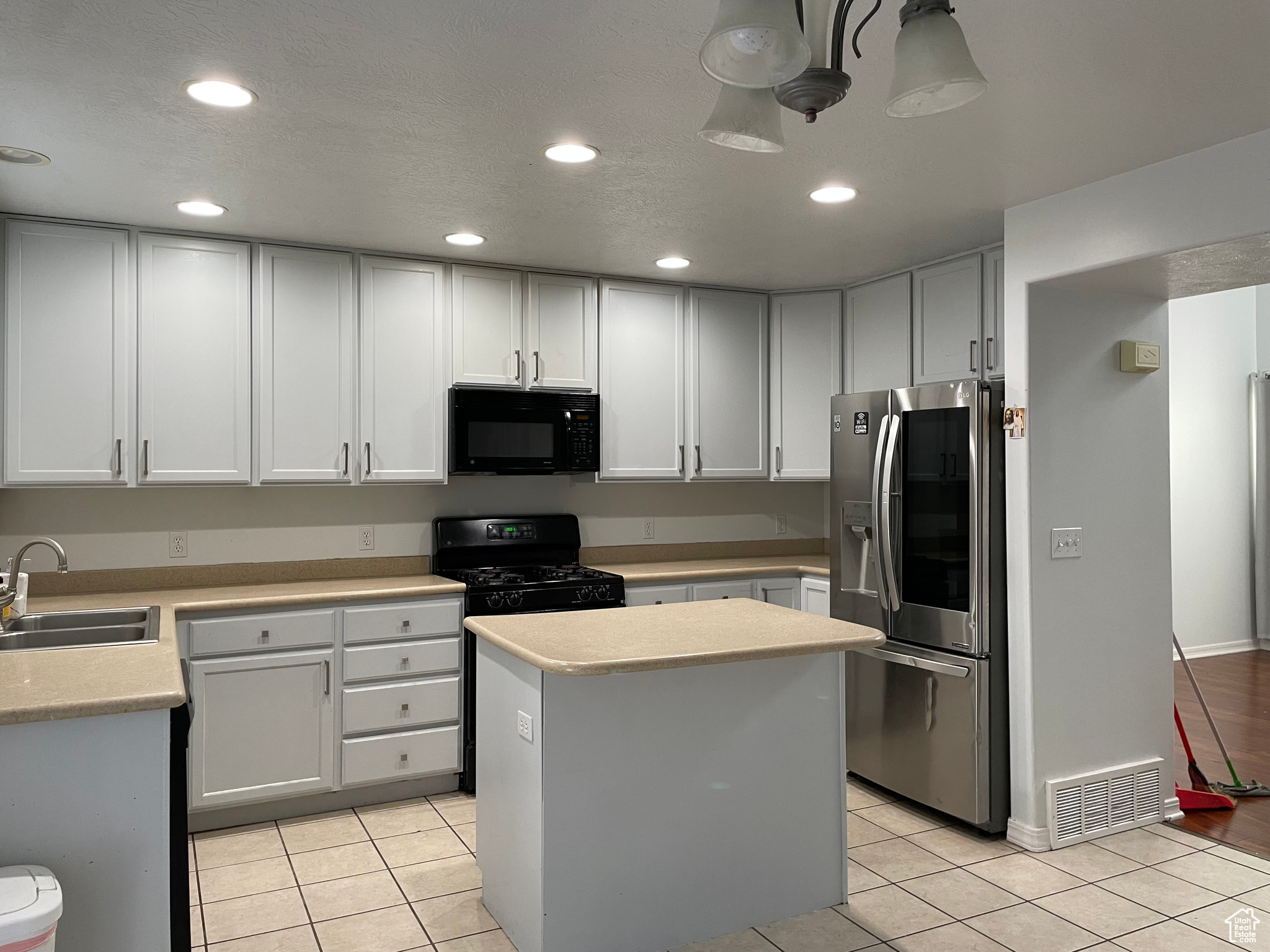 Kitchen featuring black appliances, light tile patterned floors, a center island, sink, and white cabinets