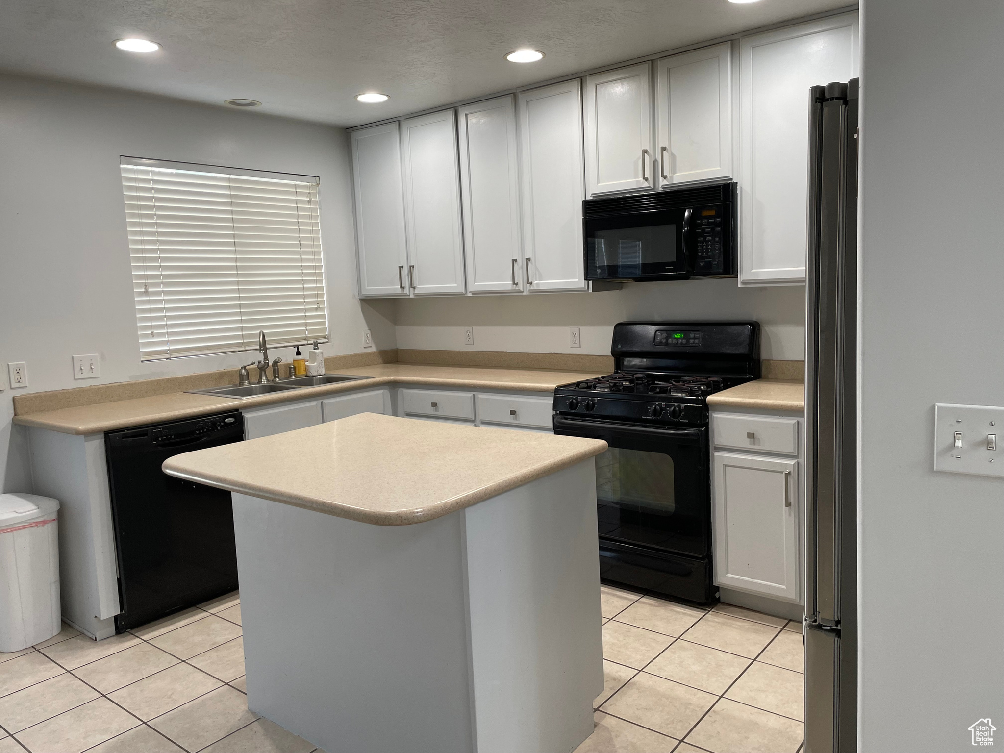 Kitchen with black appliances, white cabinetry, and sink