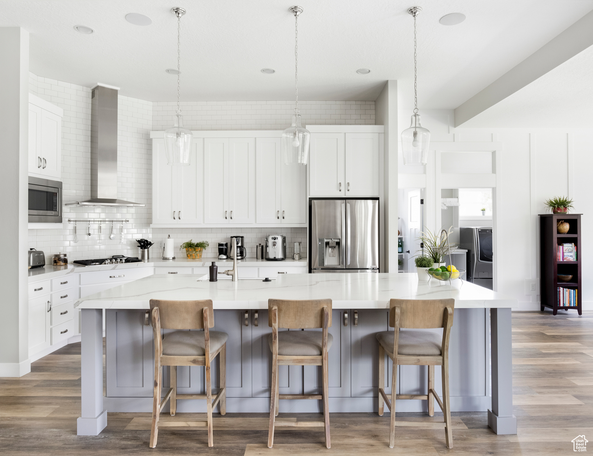 Kitchen featuring decorative light fixtures, stainless steel appliances, white cabinetry, wall chimney range hood, and a spacious island