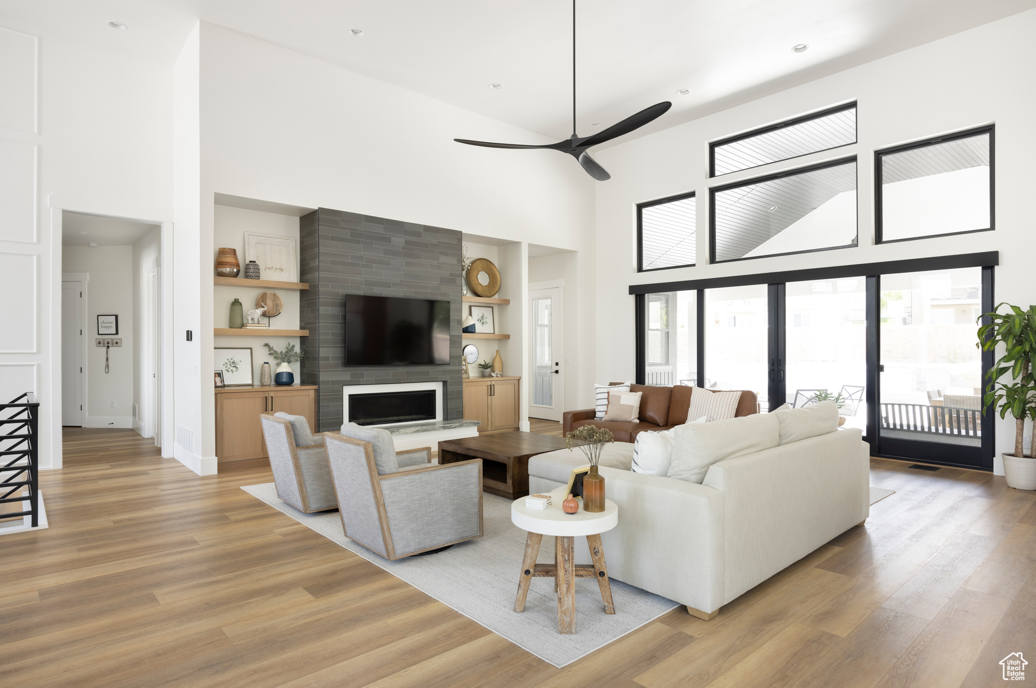 Living room with a fireplace, built in shelves, ceiling fan, a towering ceiling, and light hardwood / wood-style floors