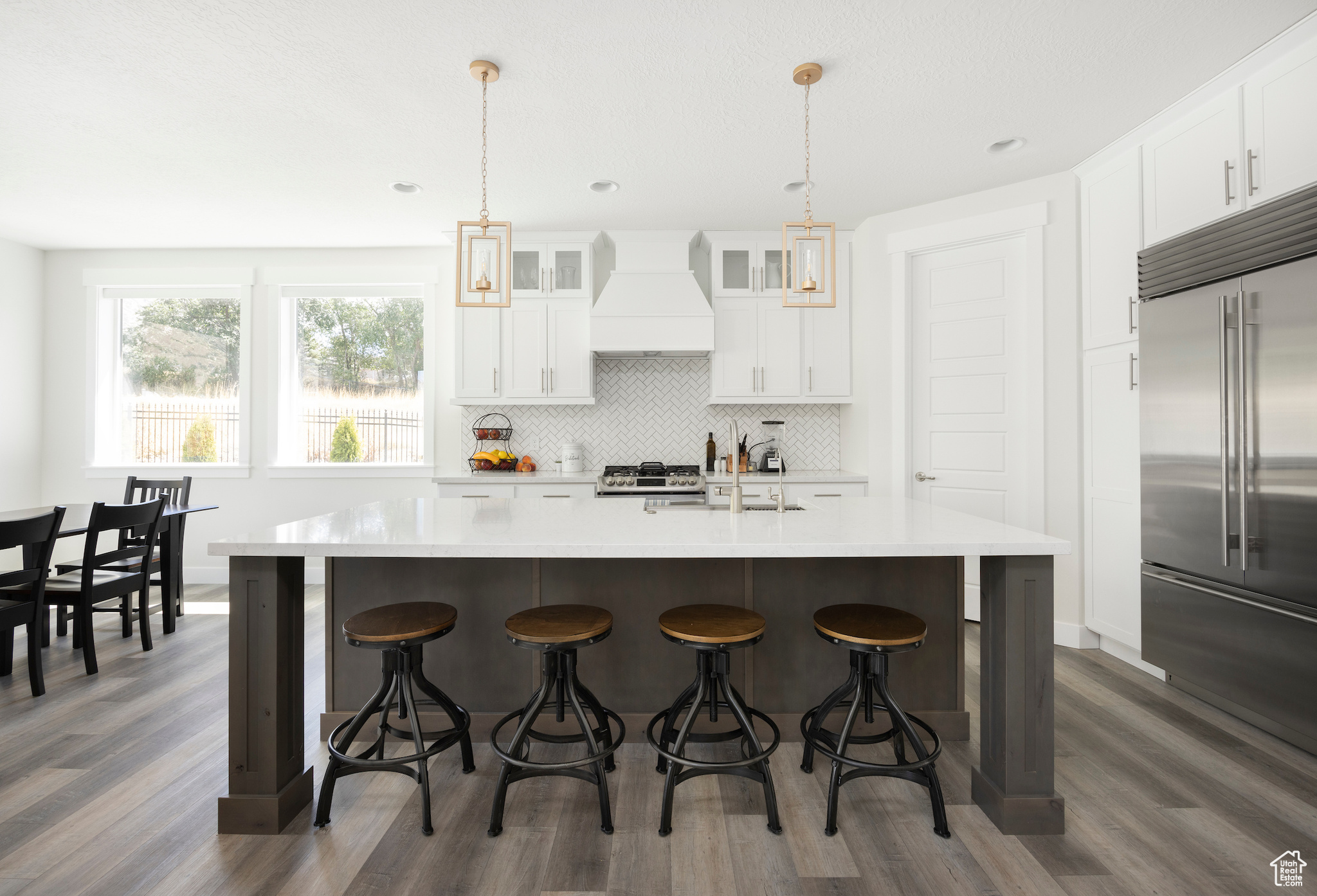 Kitchen with built in fridge, an island with sink, custom exhaust hood, and hanging light fixtures