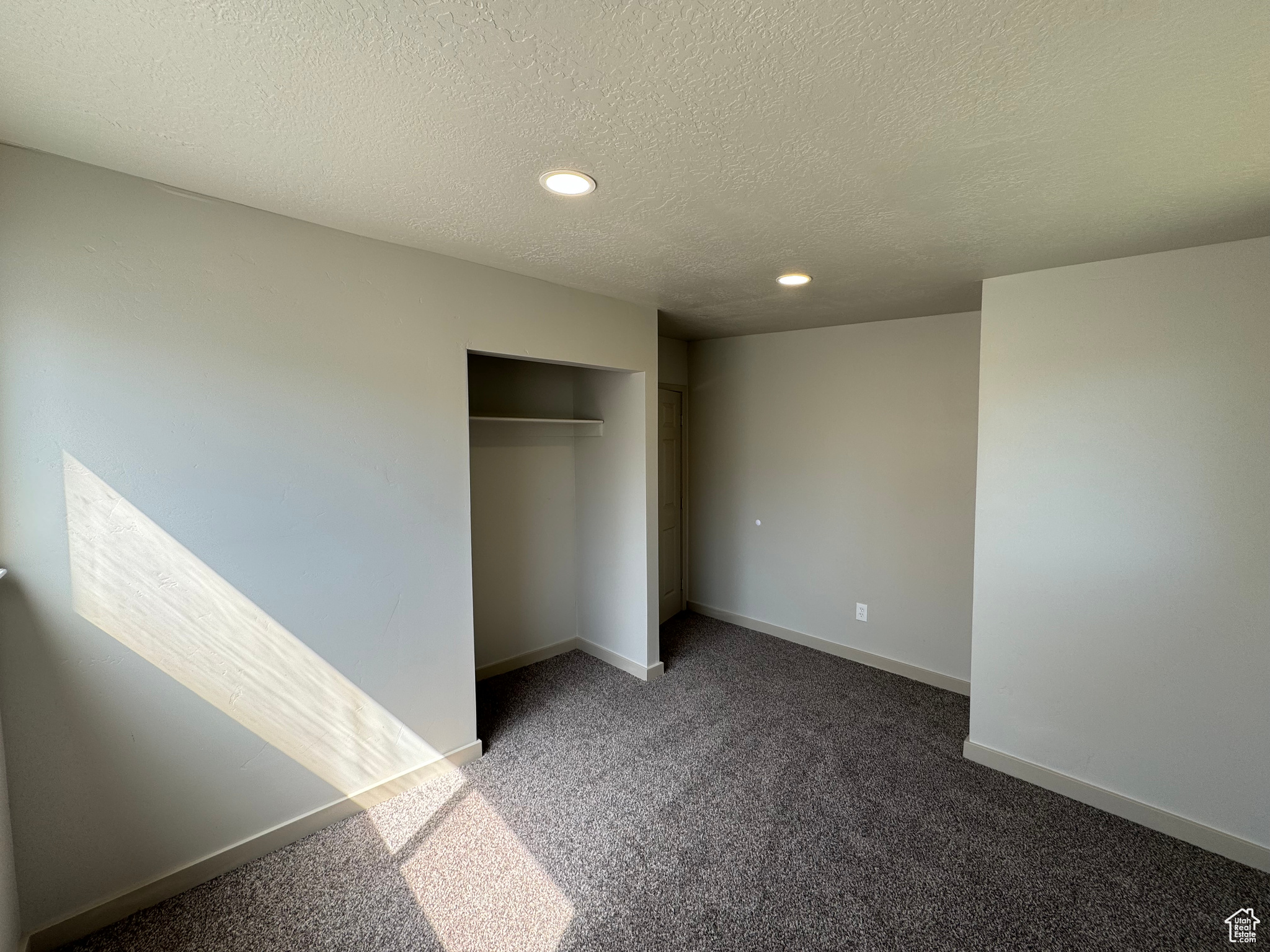 Unfurnished bedroom featuring dark carpet, a closet, and a textured ceiling