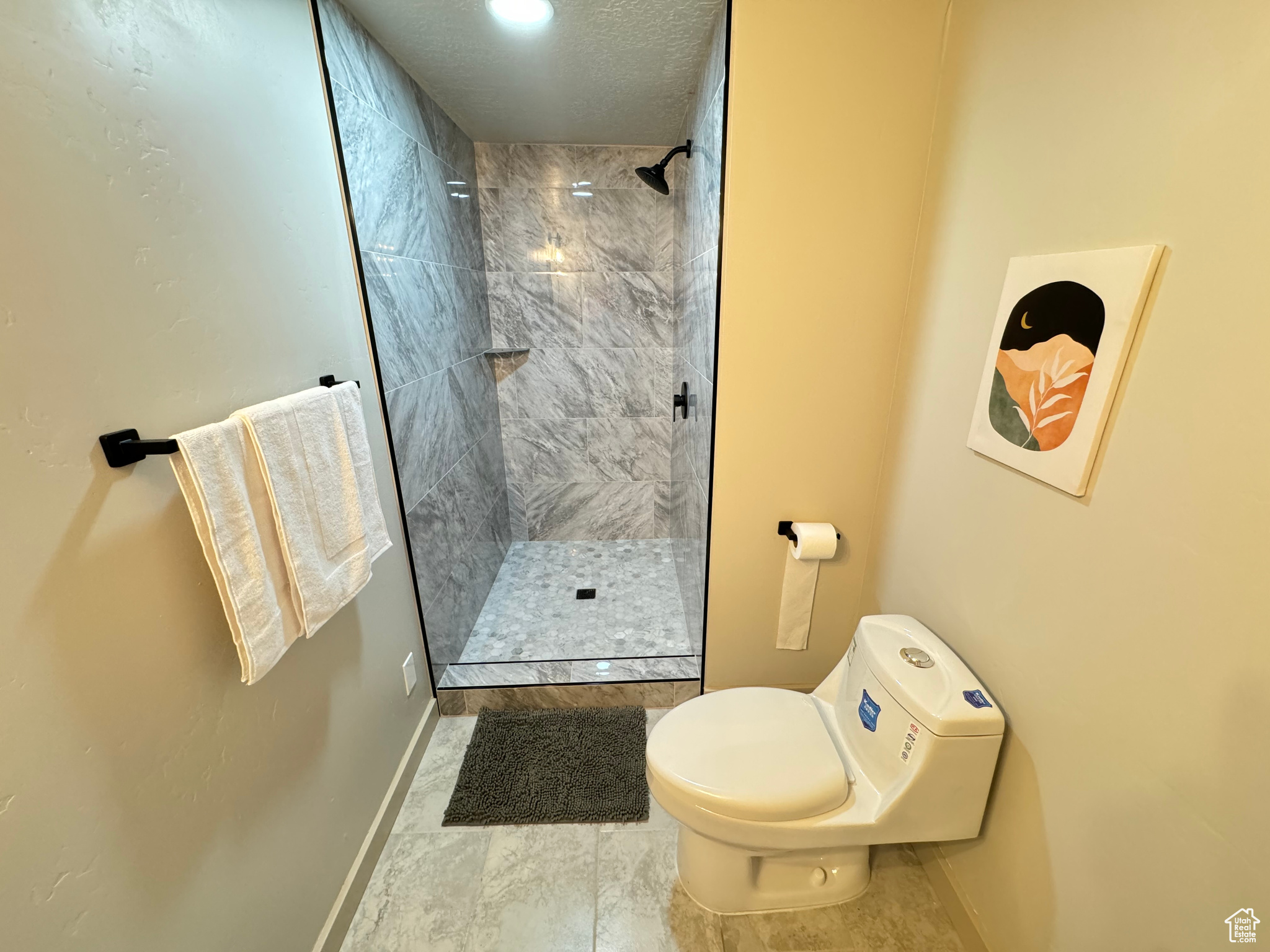 Bathroom featuring toilet, a tile shower, and tile patterned flooring