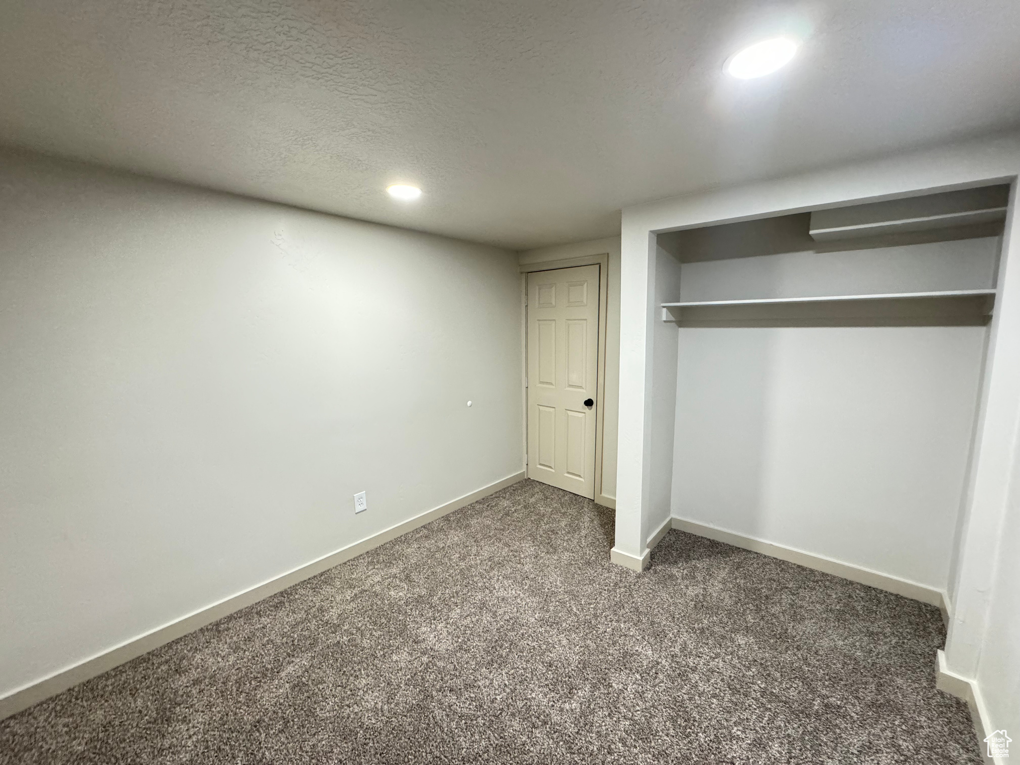 Unfurnished bedroom featuring a textured ceiling, dark carpet, and a closet