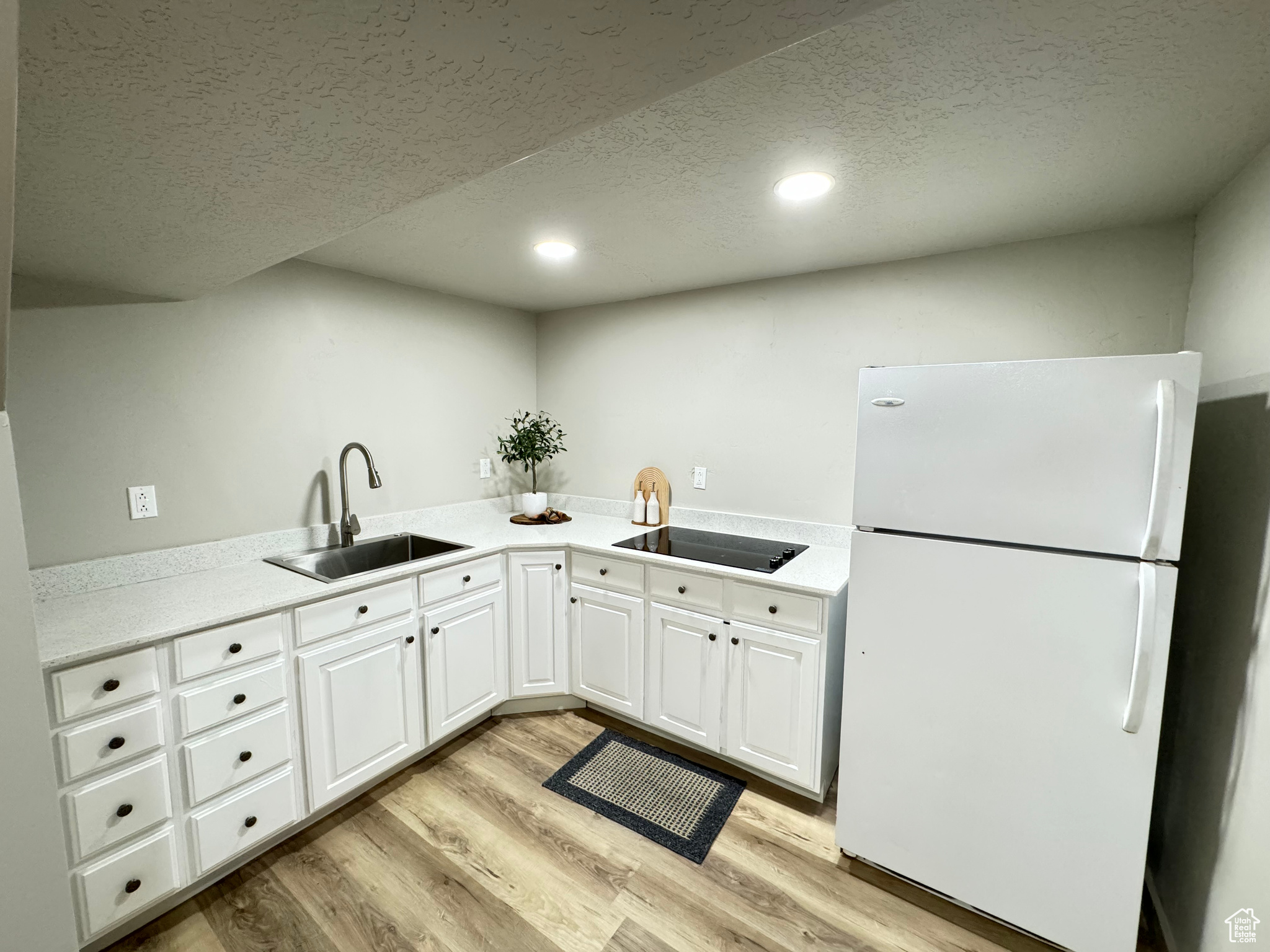 Kitchen featuring light hardwood / wood-style flooring, white refrigerator, white cabinetry, sink, and black electric cooktop