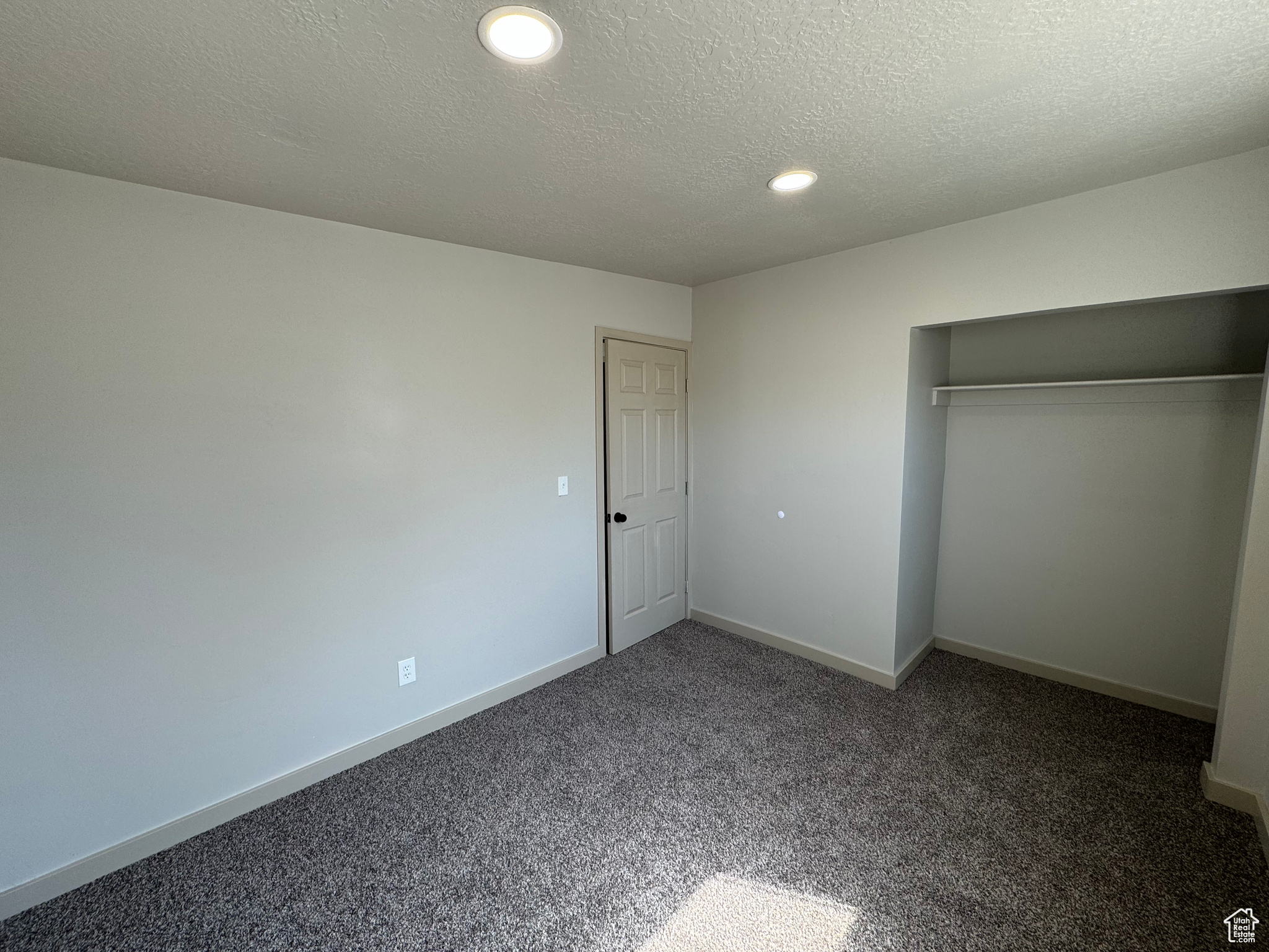 Unfurnished bedroom featuring a closet, dark colored carpet, and a textured ceiling