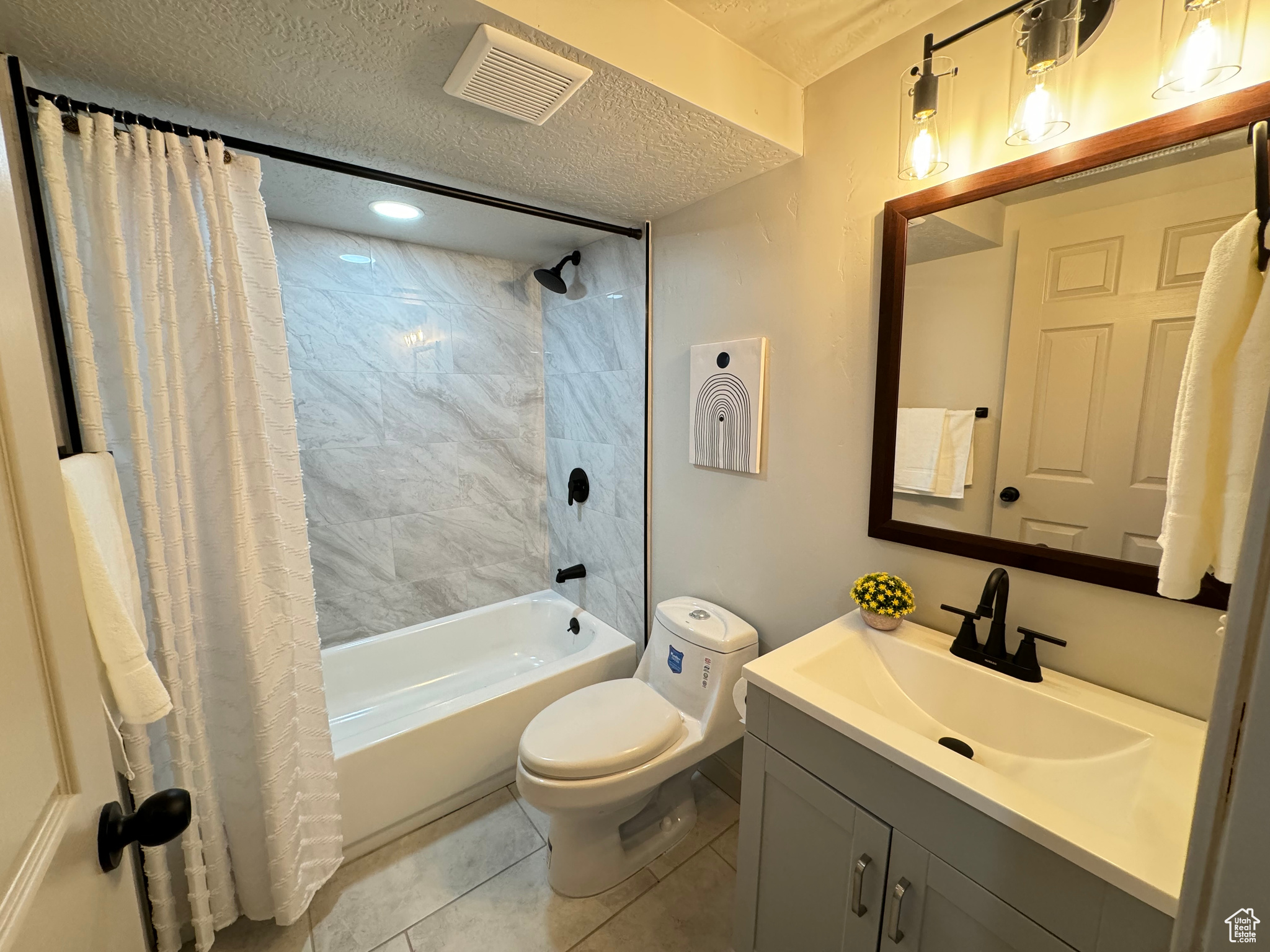 Full bathroom featuring tile patterned floors, toilet, vanity, shower / bath combo with shower curtain, and a textured ceiling