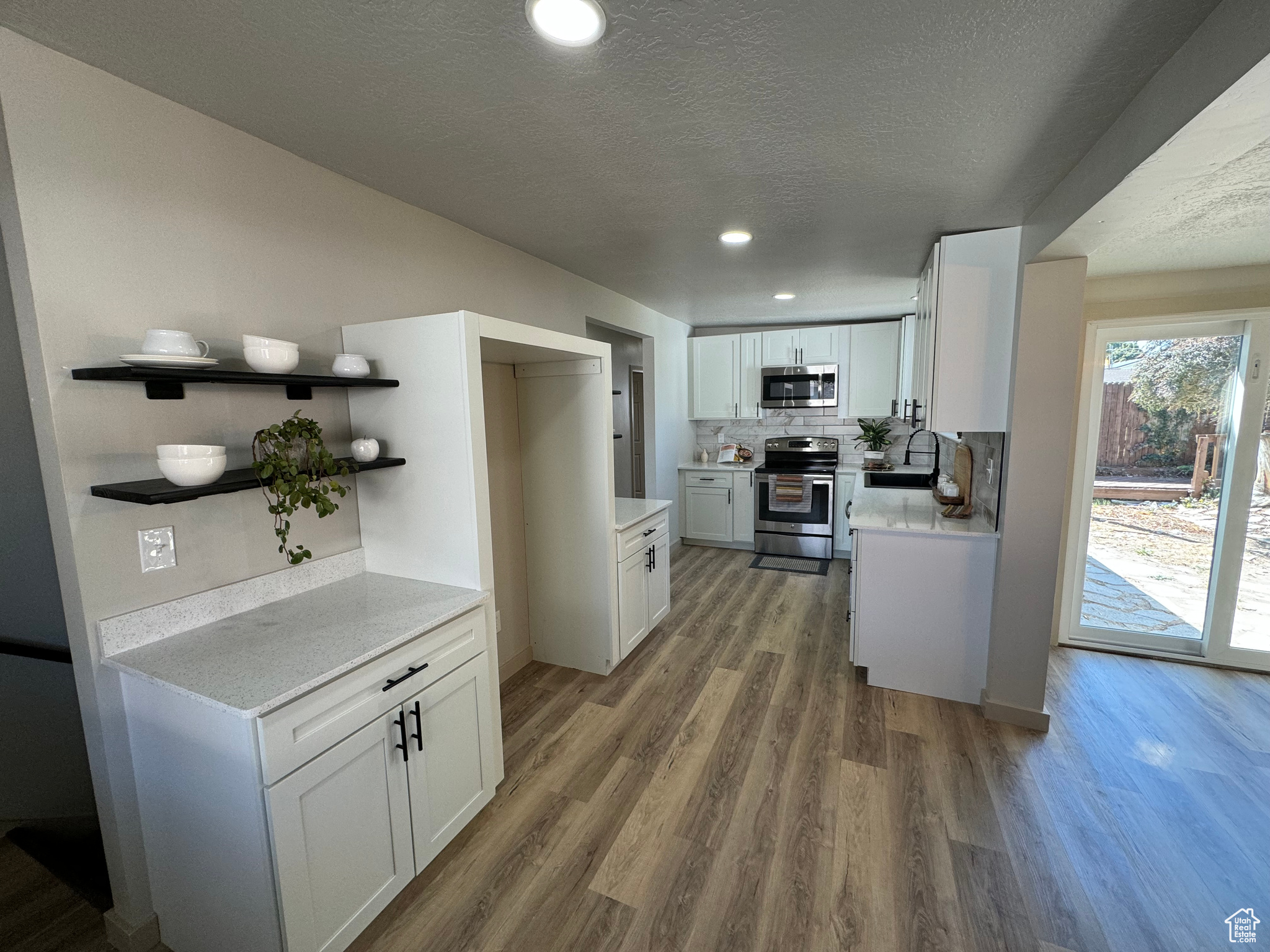 Kitchen with a textured ceiling, wood-type flooring, stainless steel appliances, sink, and white cabinetry