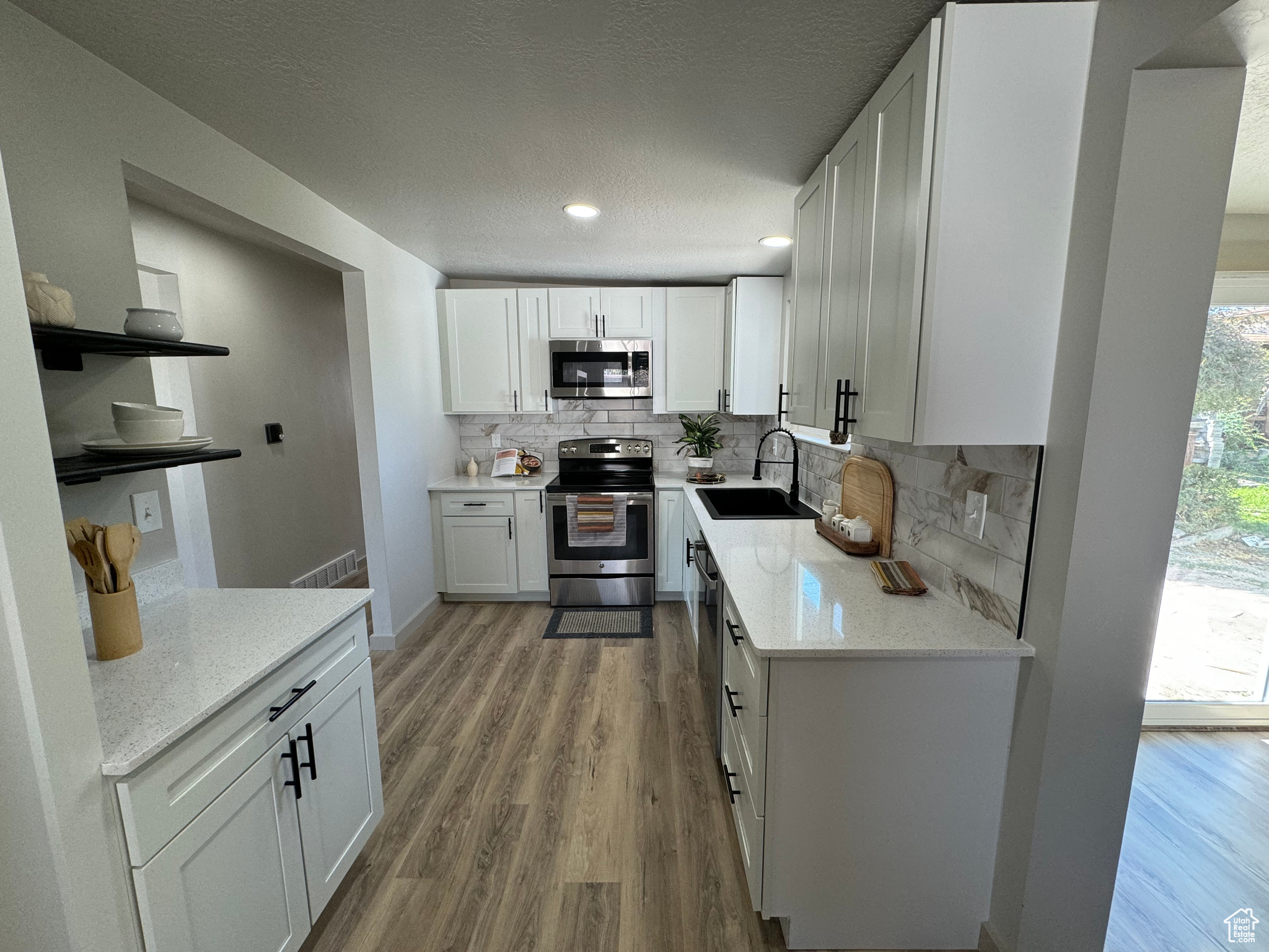 Kitchen featuring backsplash, hardwood / wood-style floors, appliances with stainless steel finishes, white cabinetry, and sink