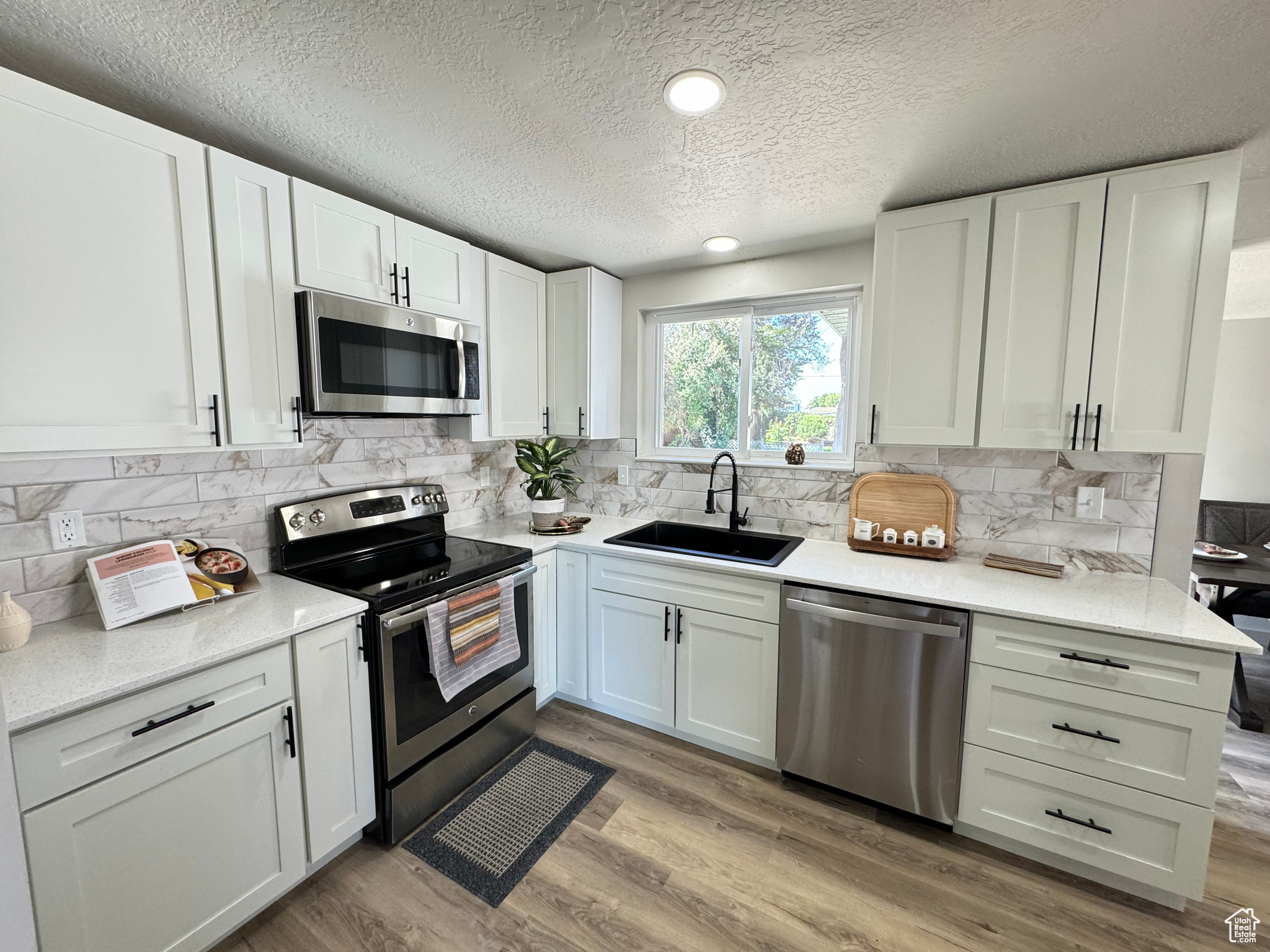 Kitchen featuring a textured ceiling, appliances with stainless steel finishes, light hardwood / wood-style floors, sink, and white cabinets