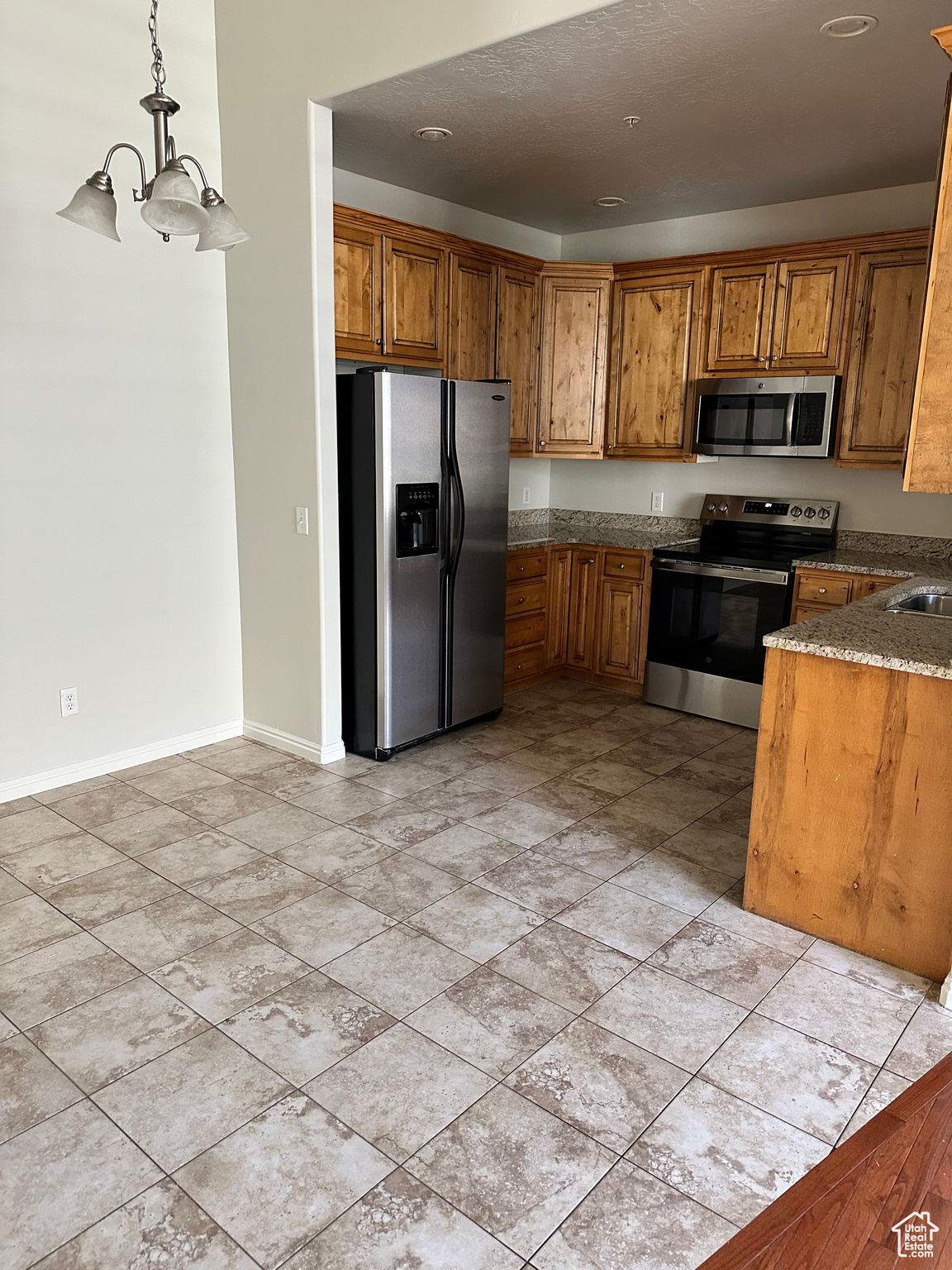 Kitchen with hanging light fixtures, an inviting chandelier, appliances with stainless steel finishes, stone countertops, and a textured ceiling