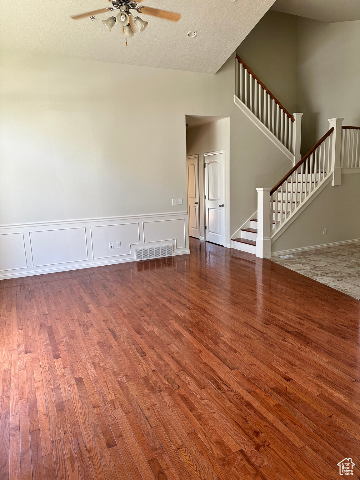 Unfurnished living room with dark wood-type flooring, high vaulted ceiling, and ceiling fan