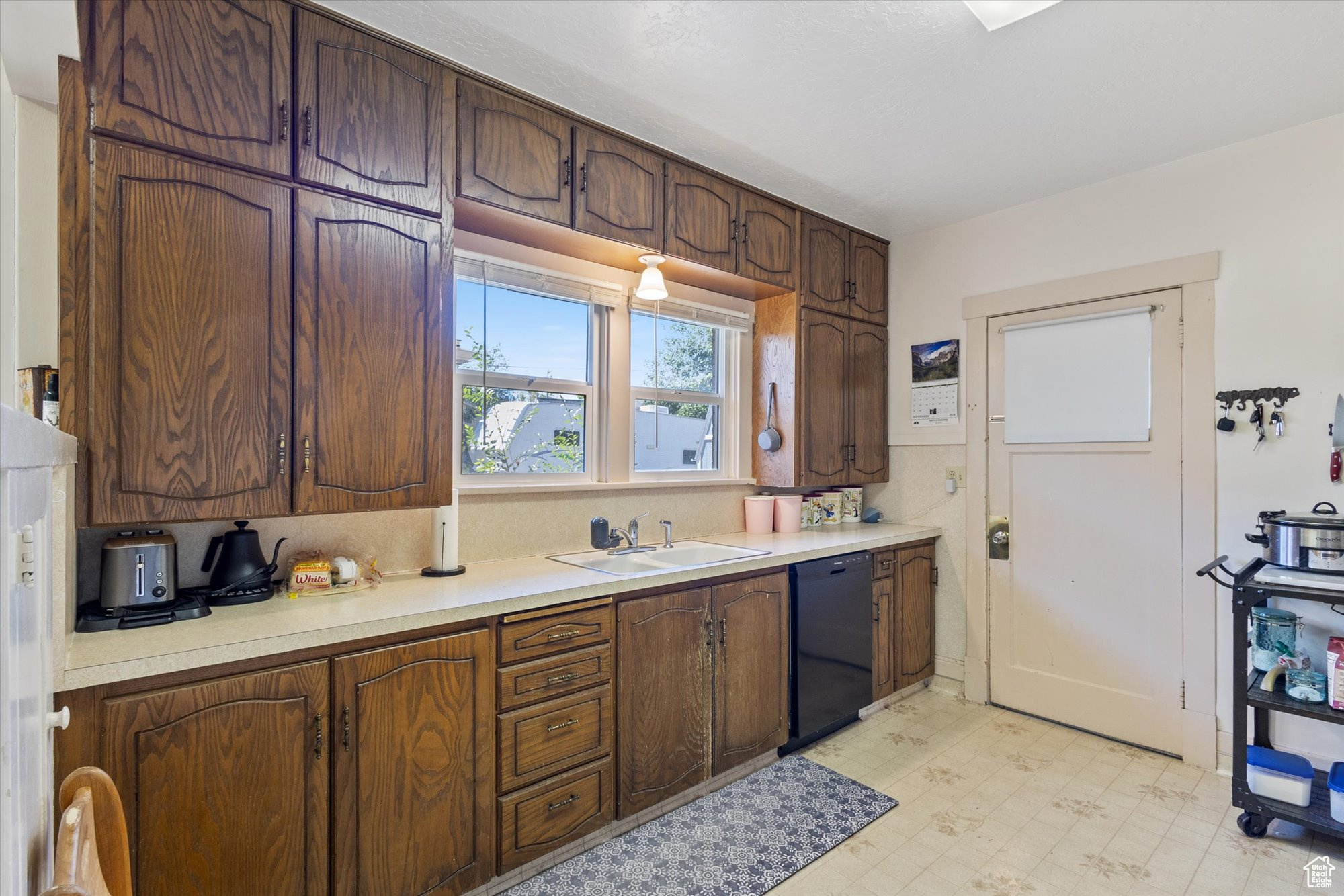 Kitchen with black dishwasher, dark brown cabinets, and sink