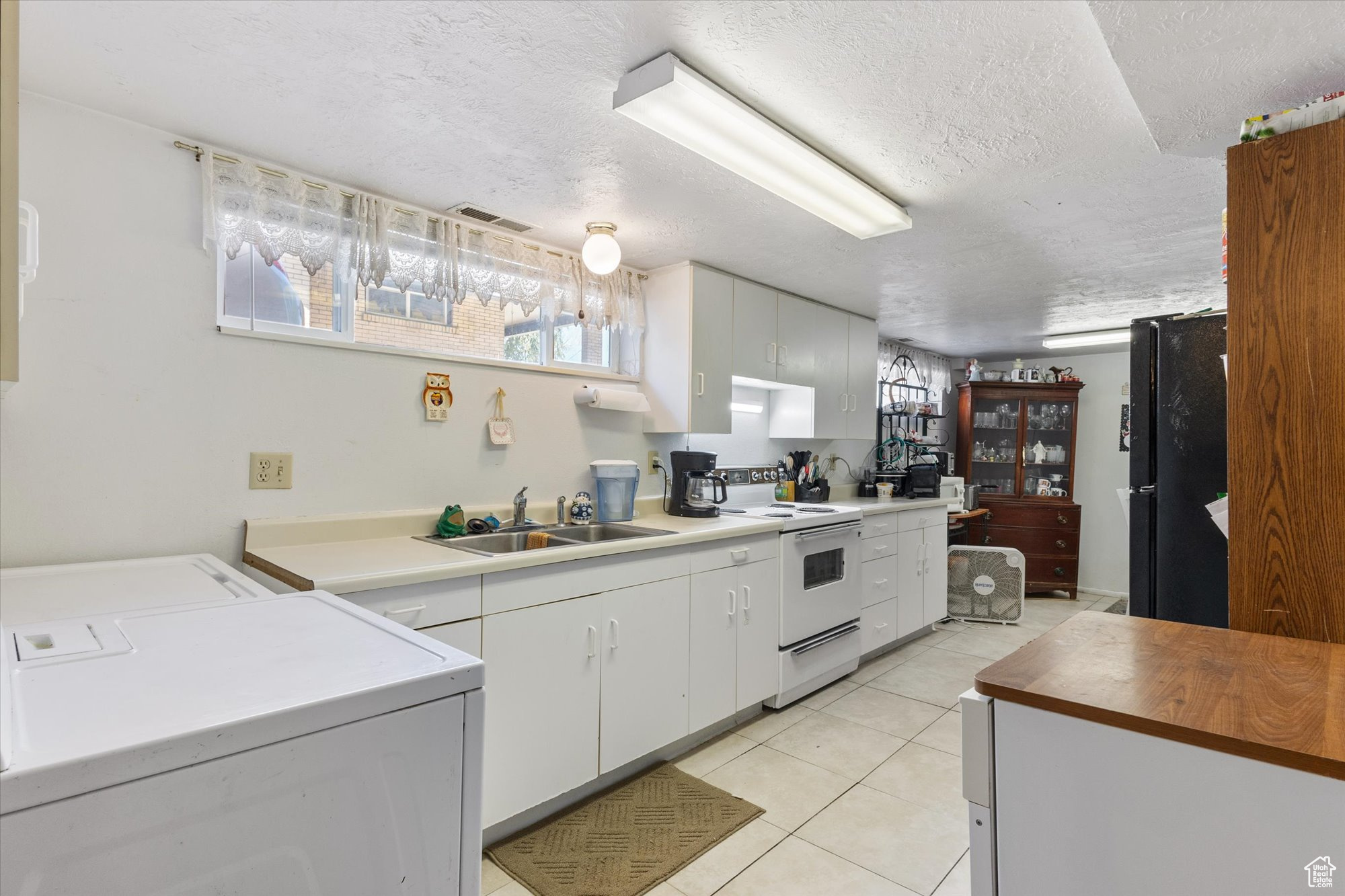 Kitchen featuring washer and clothes dryer, stove, black fridge, and white cabinets