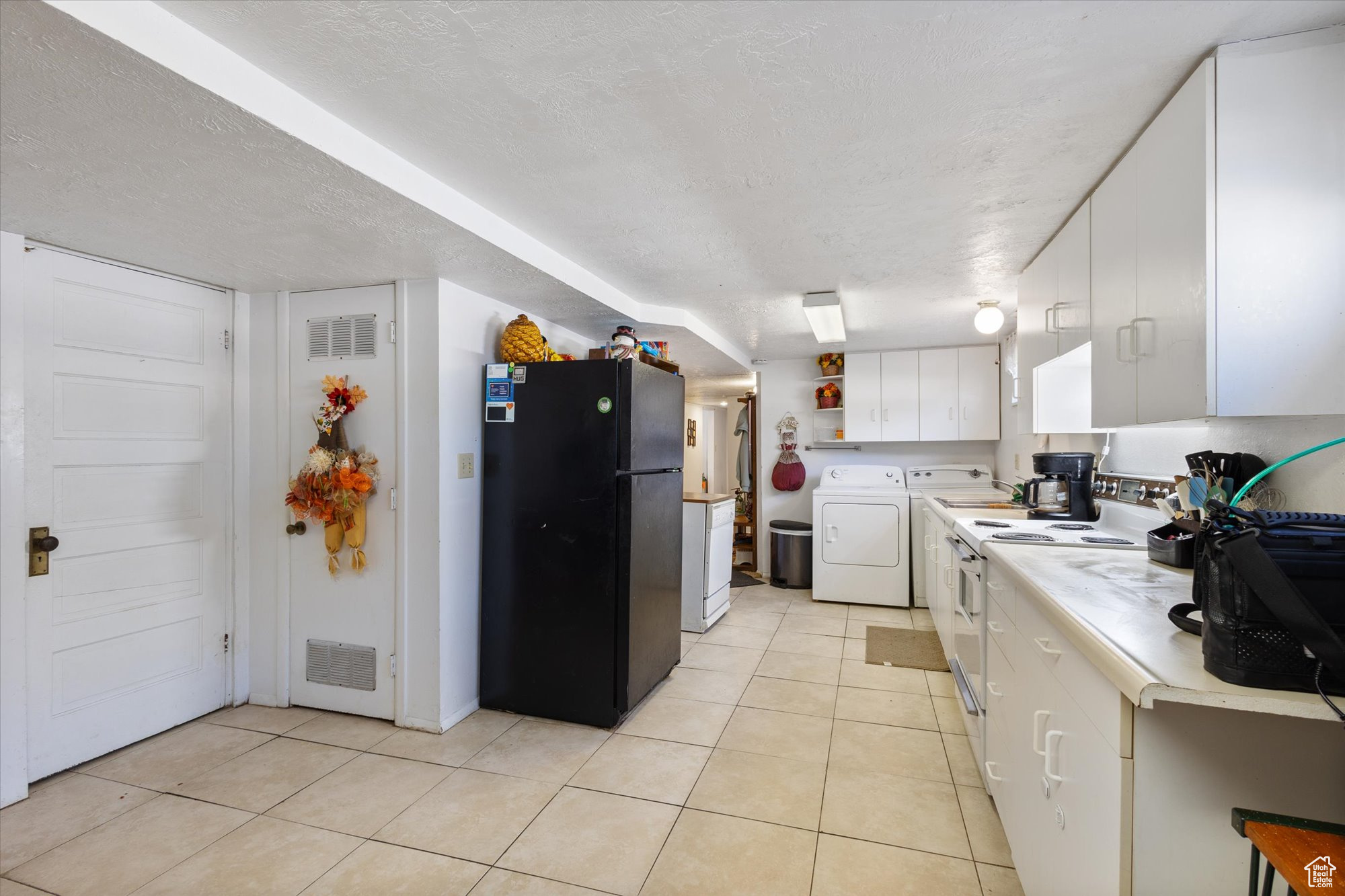 Kitchen with white cabinets, white range, black refrigerator, light tile patterned flooring, and a textured ceiling