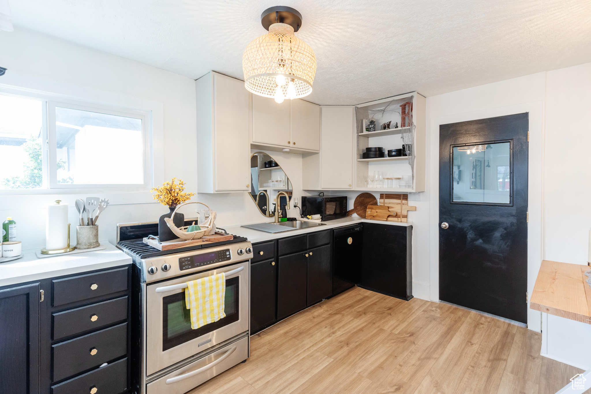 Kitchen with light hardwood / wood-style floors, sink, white cabinetry, an inviting chandelier, and black appliances