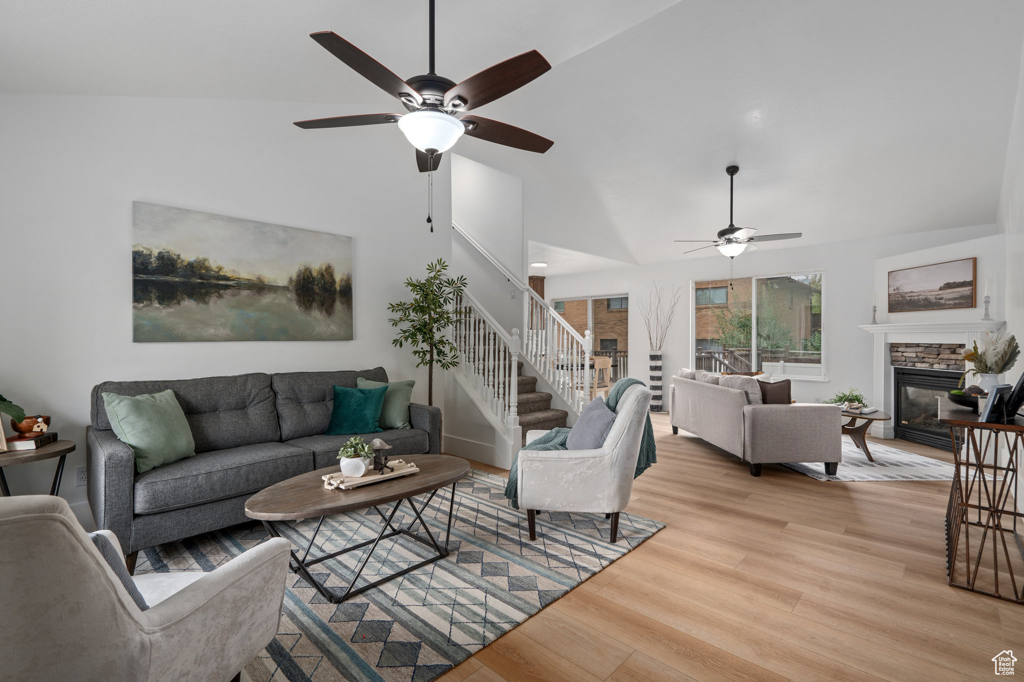 Living room with ceiling fan, a stone fireplace, light hardwood / wood-style flooring, and lofted ceiling