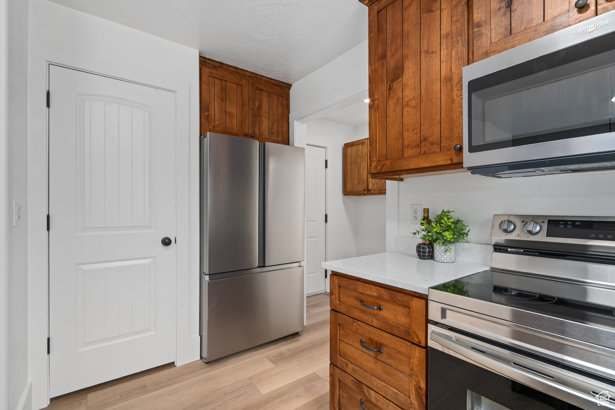 Kitchen with a textured ceiling, appliances with stainless steel finishes, and light hardwood / wood-style flooring