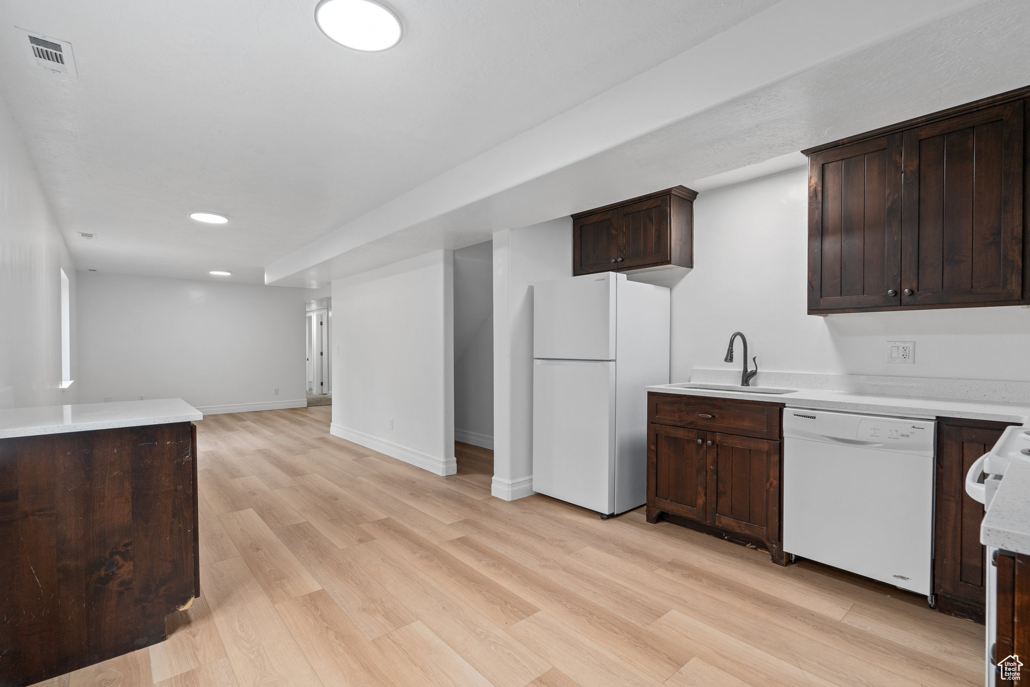 Kitchen with dark brown cabinetry, light wood-type flooring, sink, and white appliances