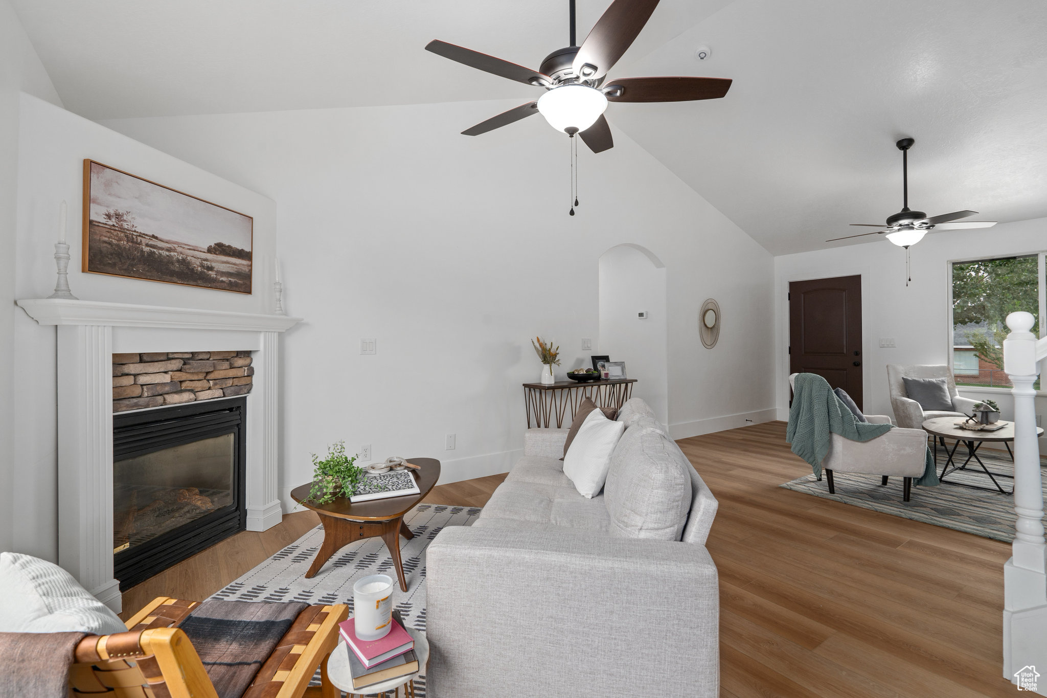 Living room featuring ceiling fan, a stone fireplace, light wood-type flooring, and vaulted ceiling