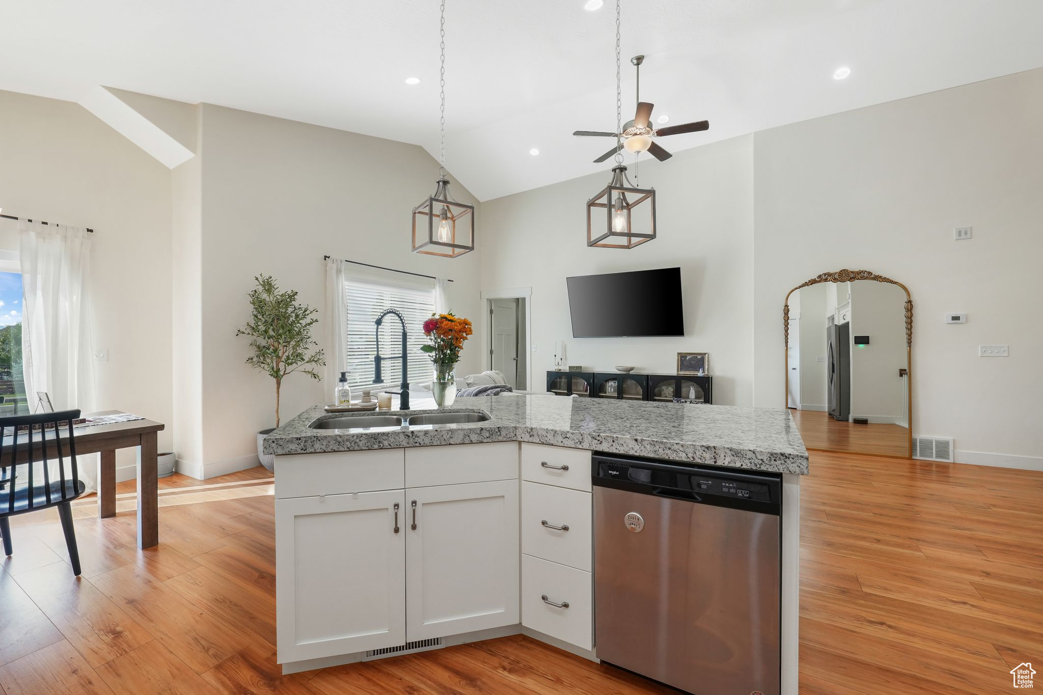 Kitchen featuring high vaulted ceiling, white cabinetry, sink, stainless steel dishwasher, and light hardwood / wood-style floors