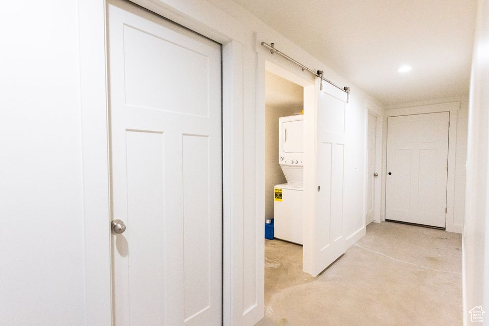 Hallway with light colored carpet, a barn door, and stacked washing maching and dryer