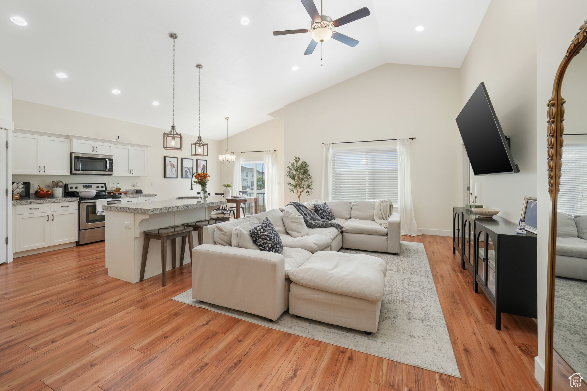 Living room with light wood-type flooring, ceiling fan with notable chandelier, and high vaulted ceiling