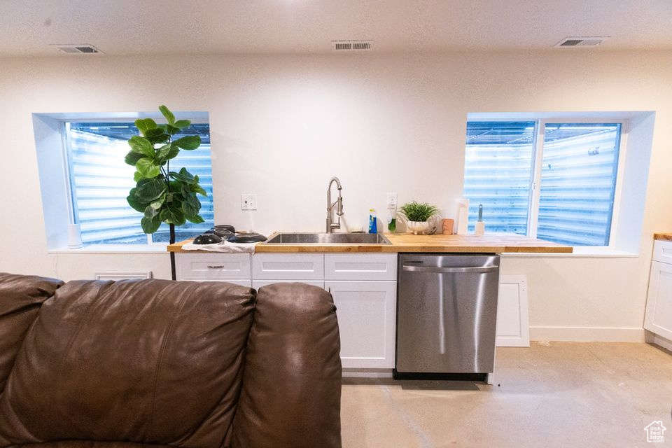 Kitchen featuring white cabinets, butcher block counters, dishwasher, sink, and light colored carpet