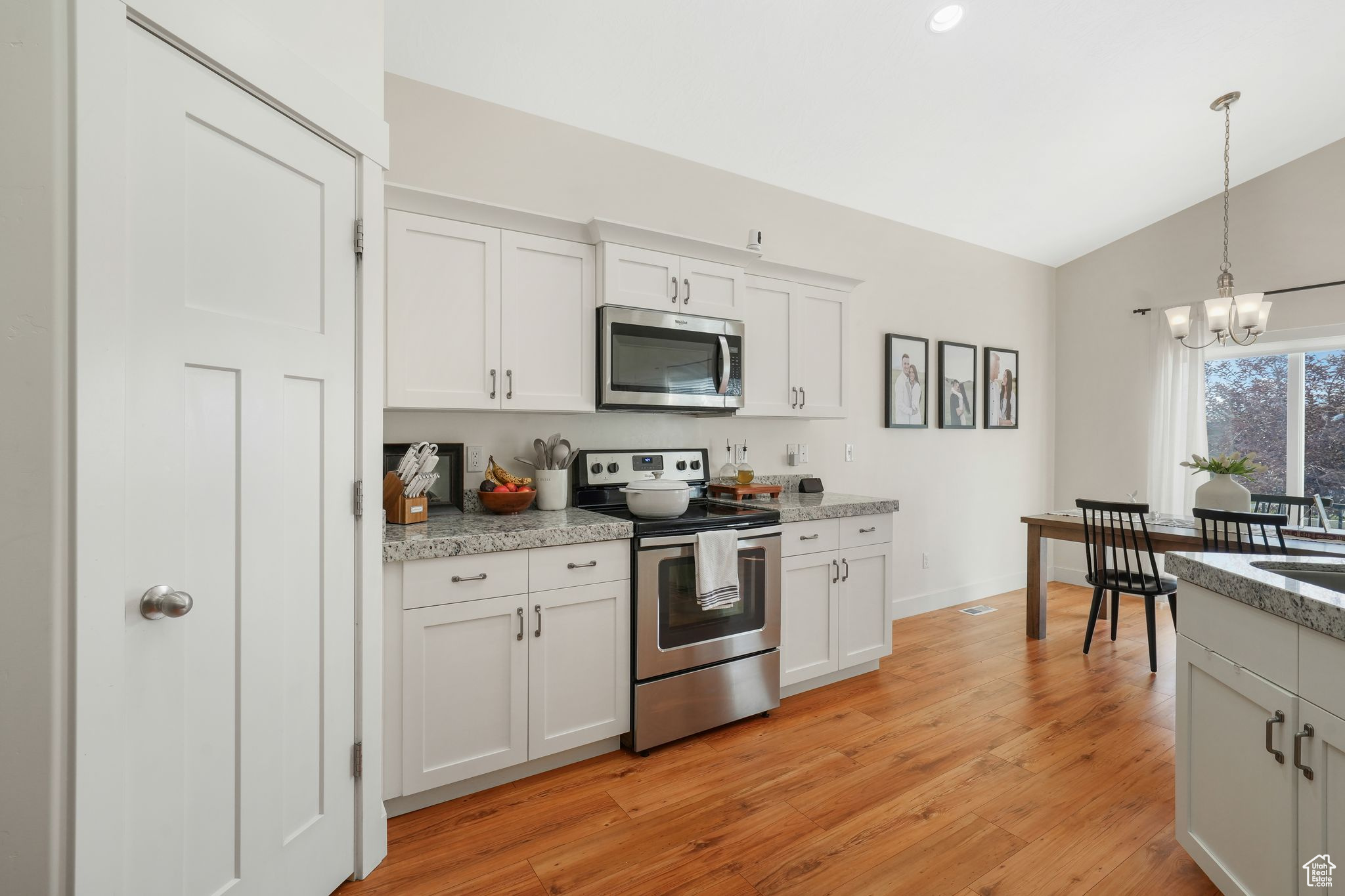 Kitchen featuring a notable chandelier, vaulted ceiling, appliances with stainless steel finishes, white cabinets, and light hardwood / wood-style floors