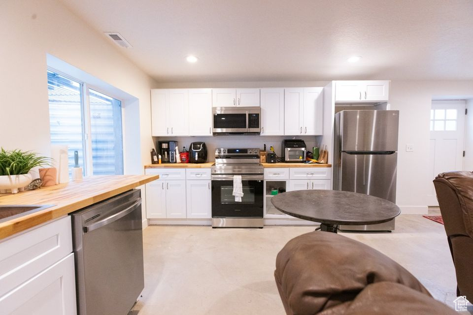 Kitchen with white cabinets, appliances with stainless steel finishes, and butcher block counters