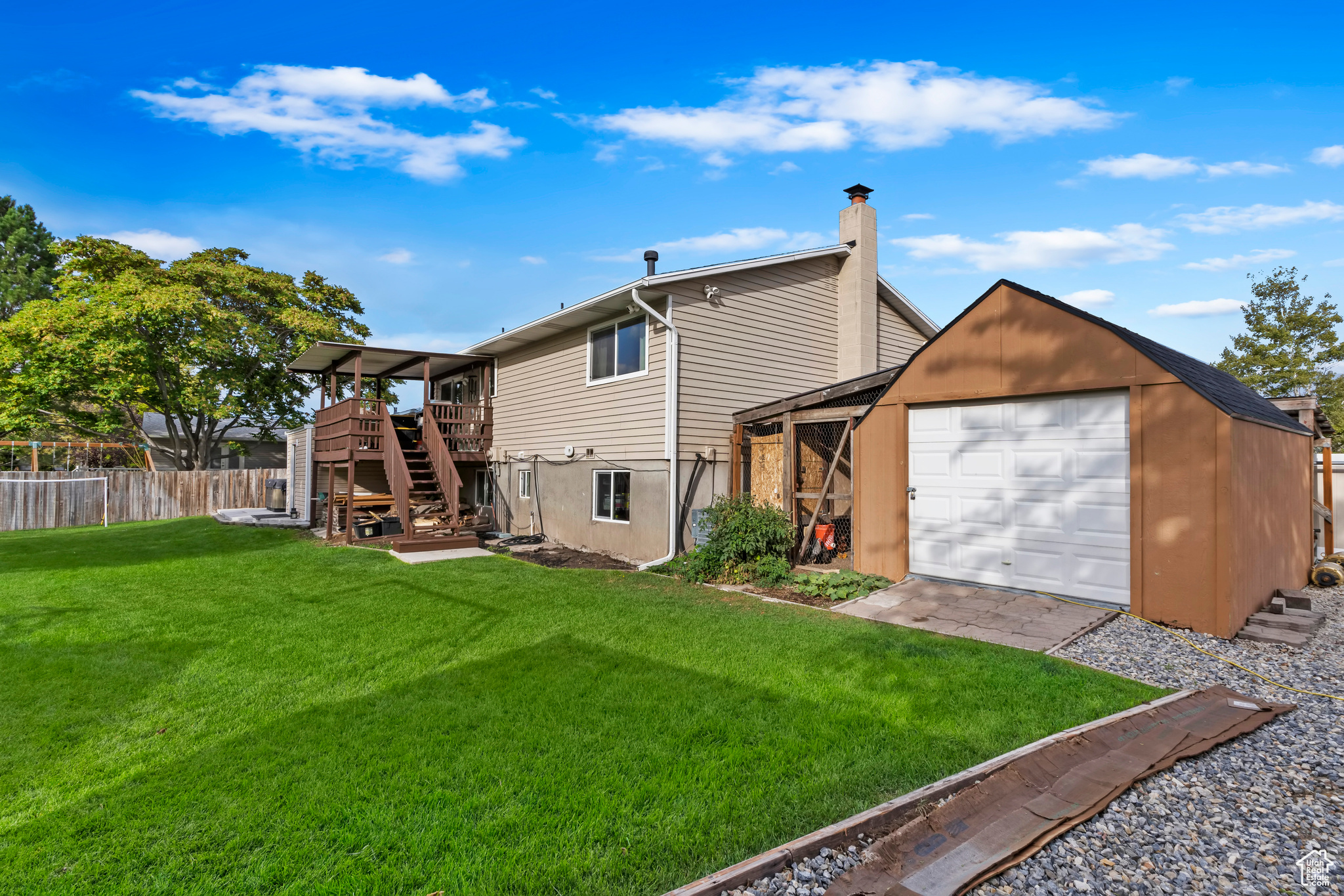 Back of house with a garage, a deck, a lawn, and an outbuilding