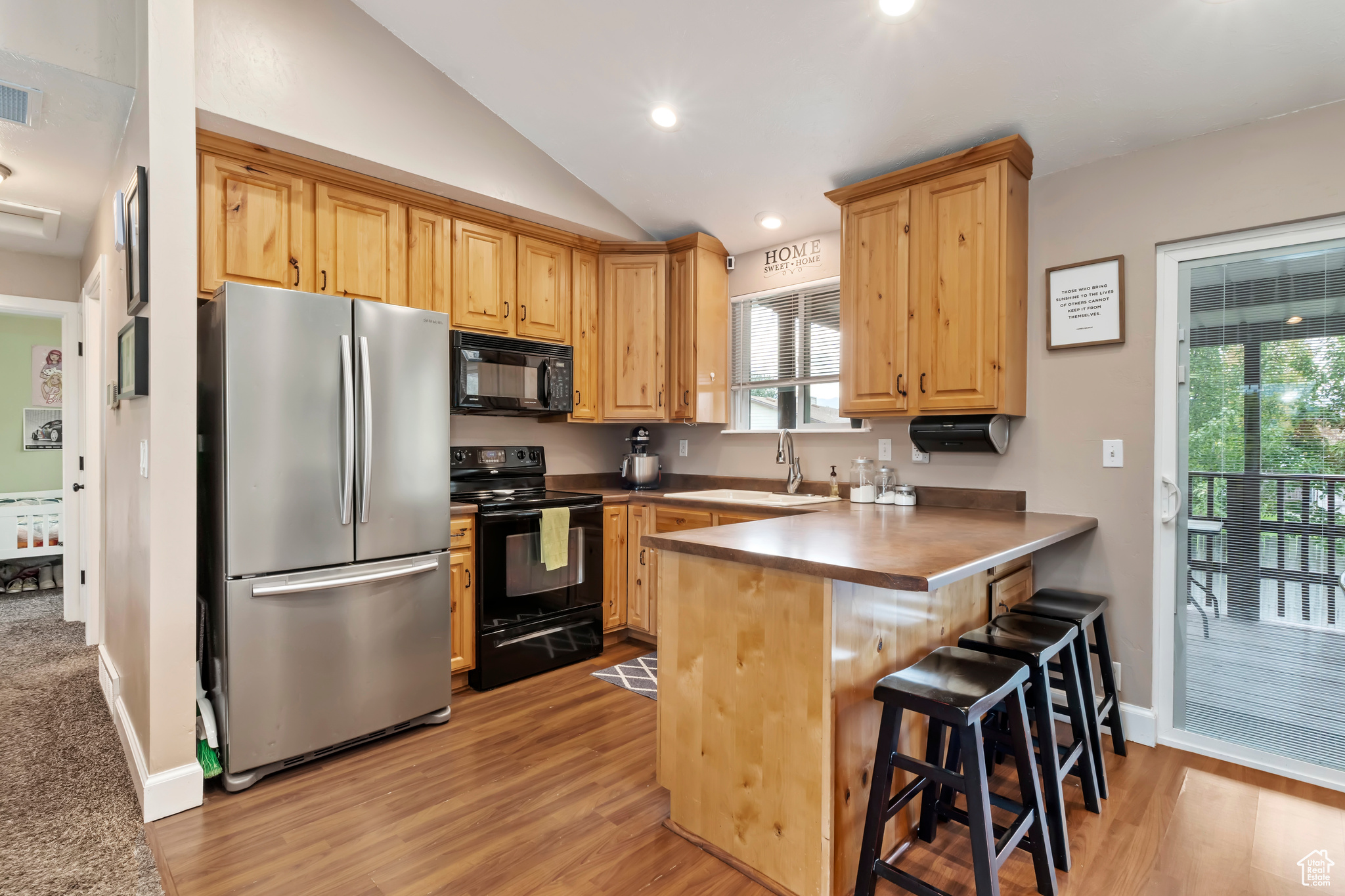 Kitchen with light hardwood / wood-style floors, a breakfast bar, kitchen peninsula, black appliances, and lofted ceiling