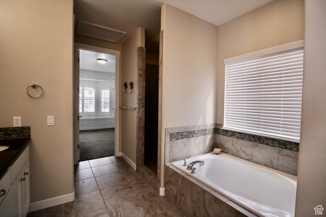 Bathroom with tile patterned floors, a relaxing tiled tub, and vanity