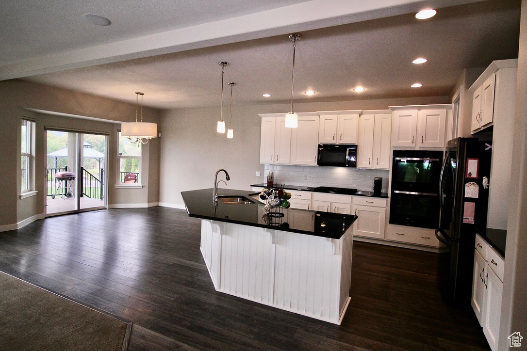 Kitchen includes a walk-out deck, an island with sink, black appliances, pendant lighting, and white cabinets