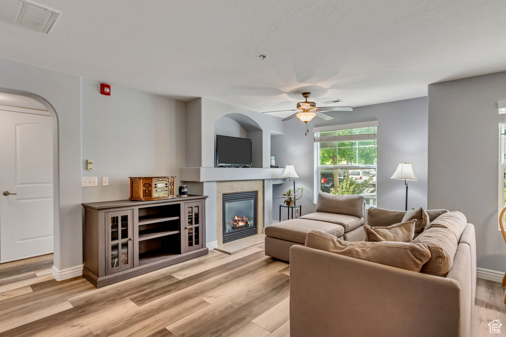 Living room with light hardwood / wood-style flooring, ceiling fan, and a tile fireplace