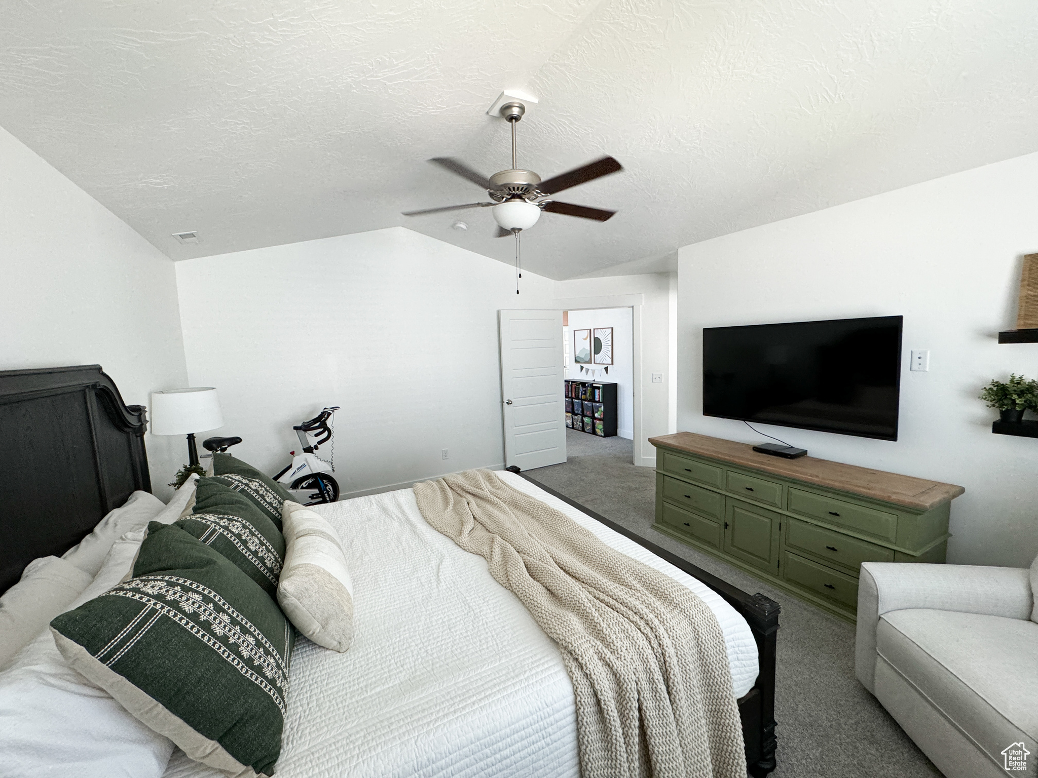 Carpeted bedroom with a textured ceiling, vaulted ceiling, and ceiling fan